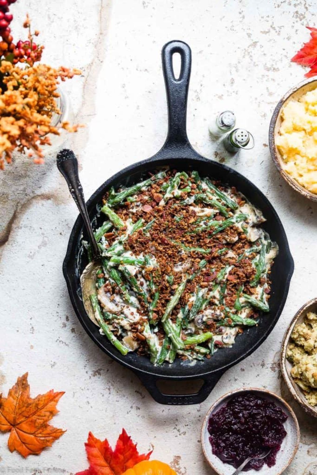 A cast iron skillet filled with green bean casserole, sprinkles with bacon crumble.