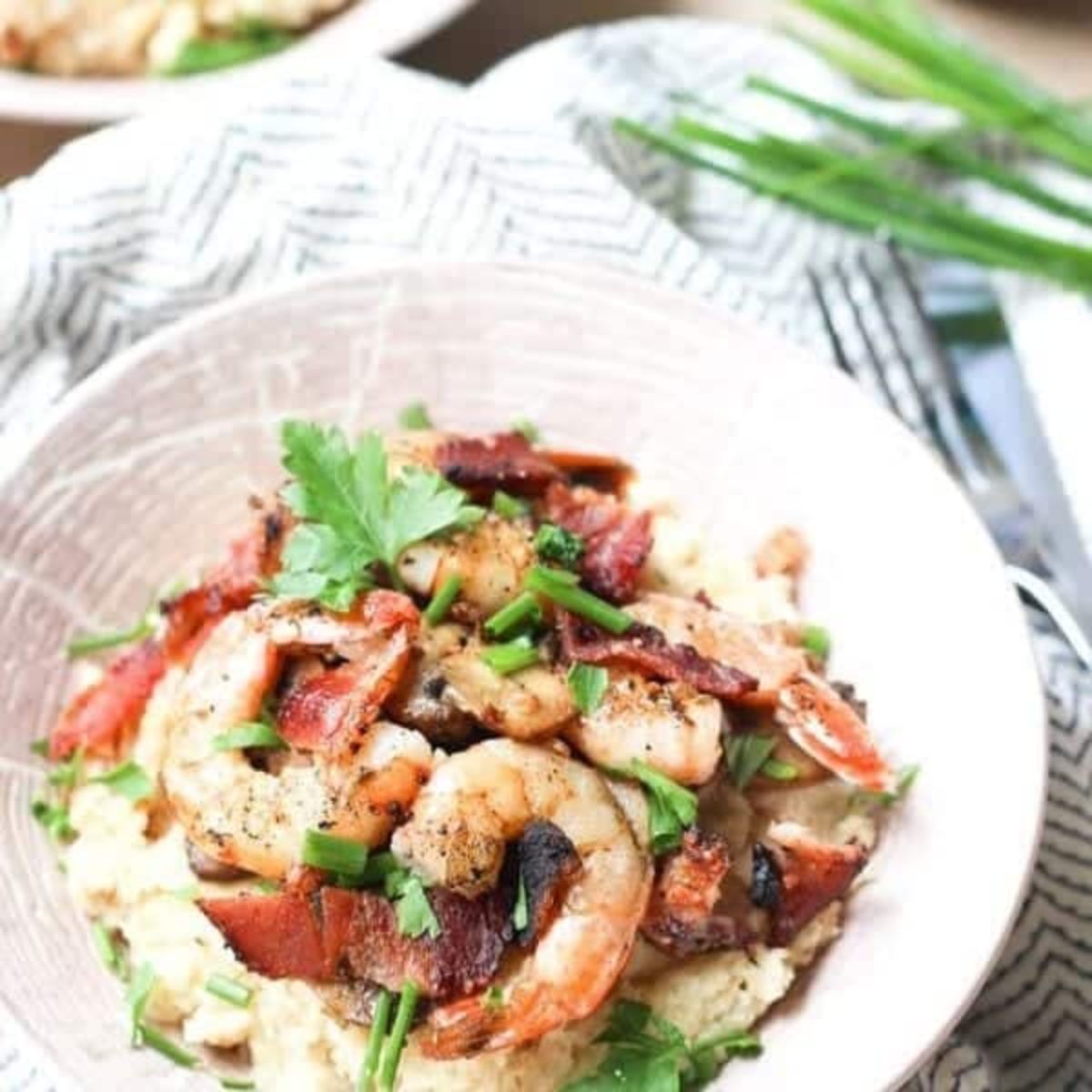 a bowl of shrimp, mash and crispy bacon with chopped herb garnish