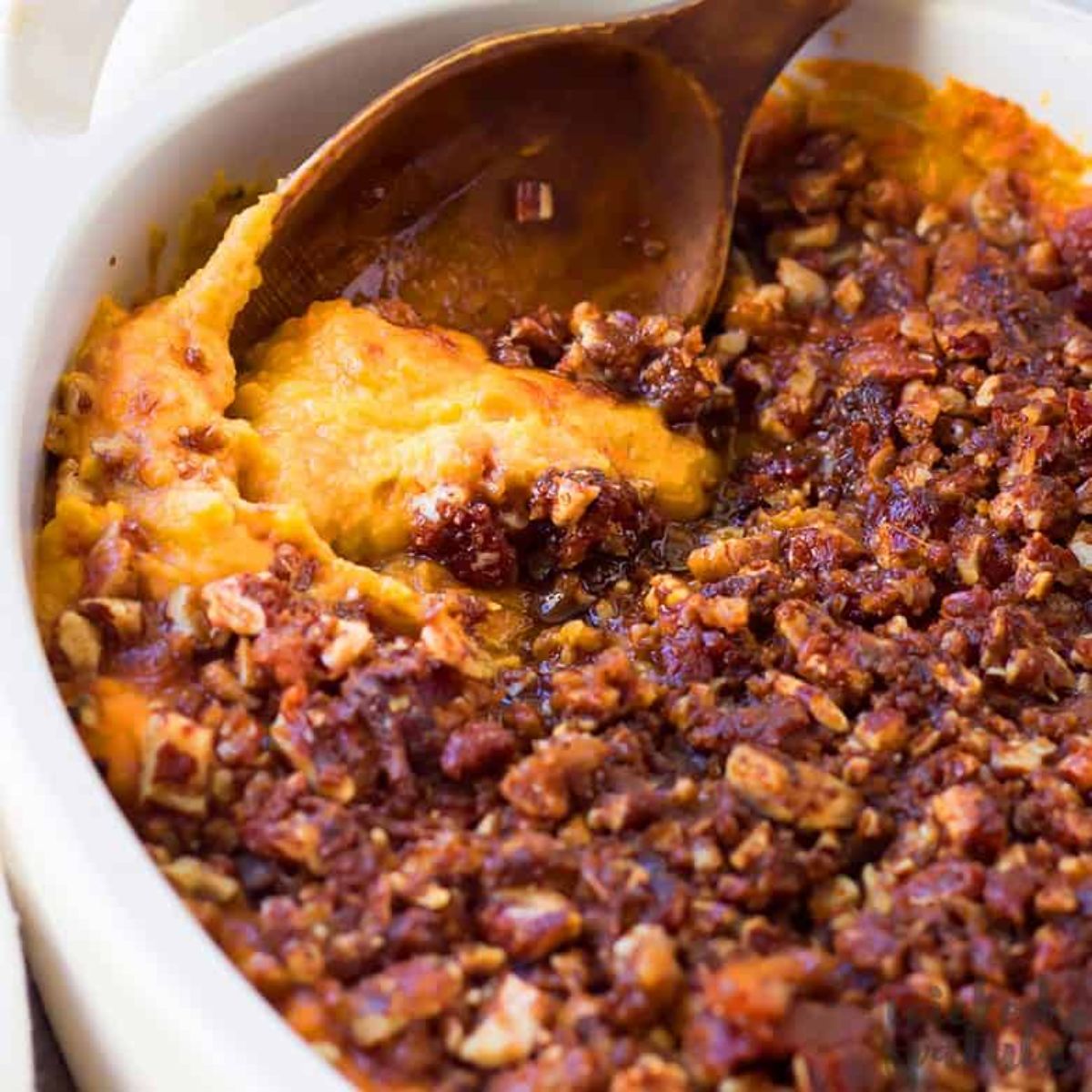 a partial shot of a casserole dish filled with sweet potato casserole, a wooden spoon is sticking out of it