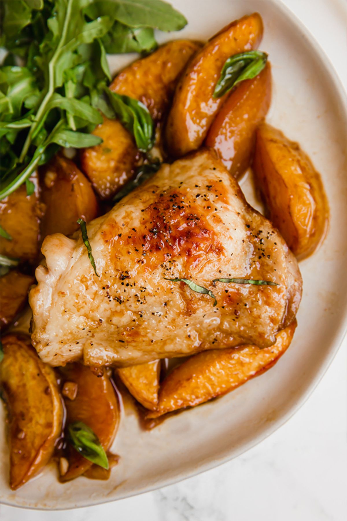 a partial shot of a plate of chicken thighs, sliced peaches and arugula