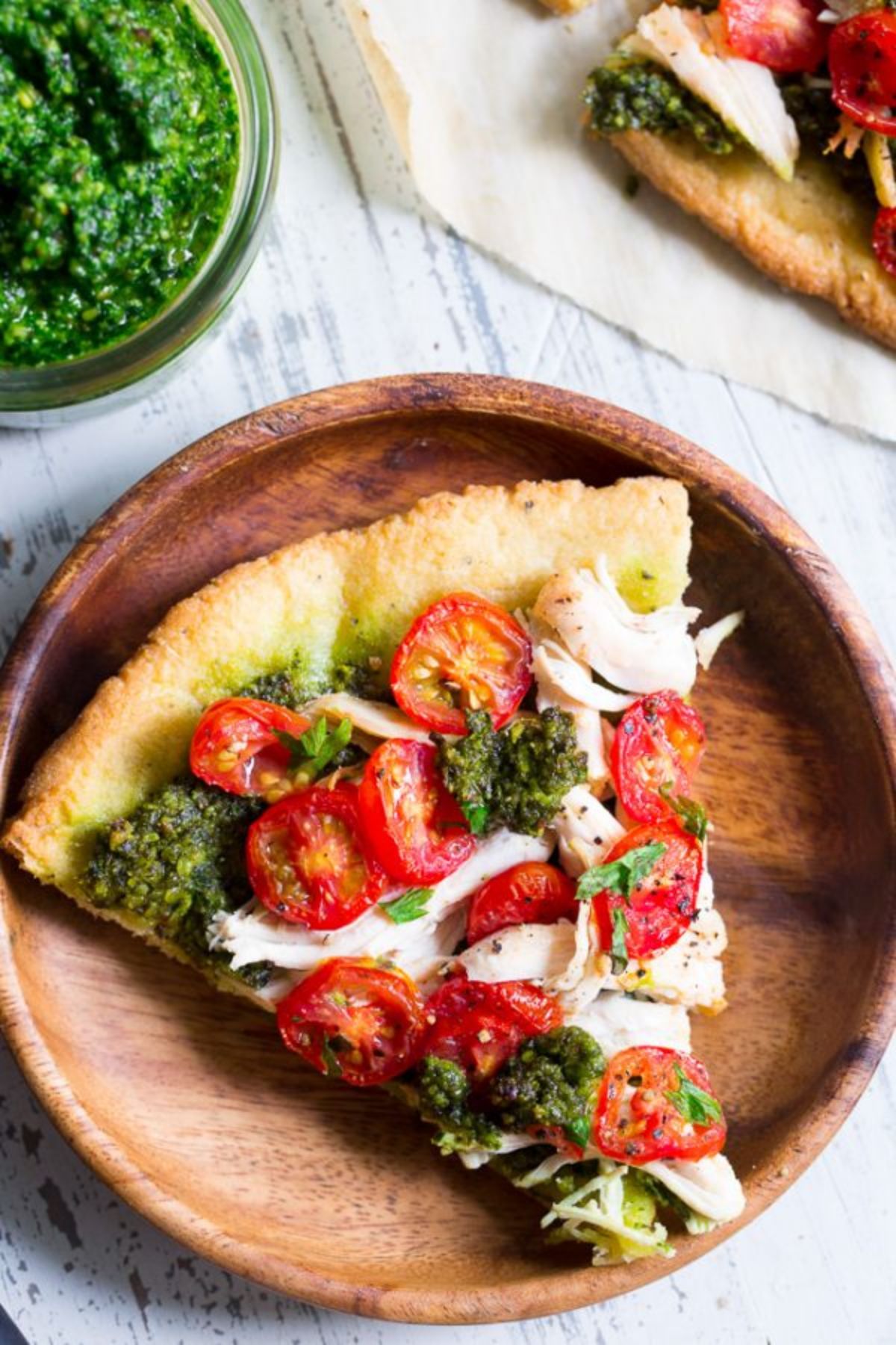 a wooden palte with a slice of tomato, pesto and chicken pizza