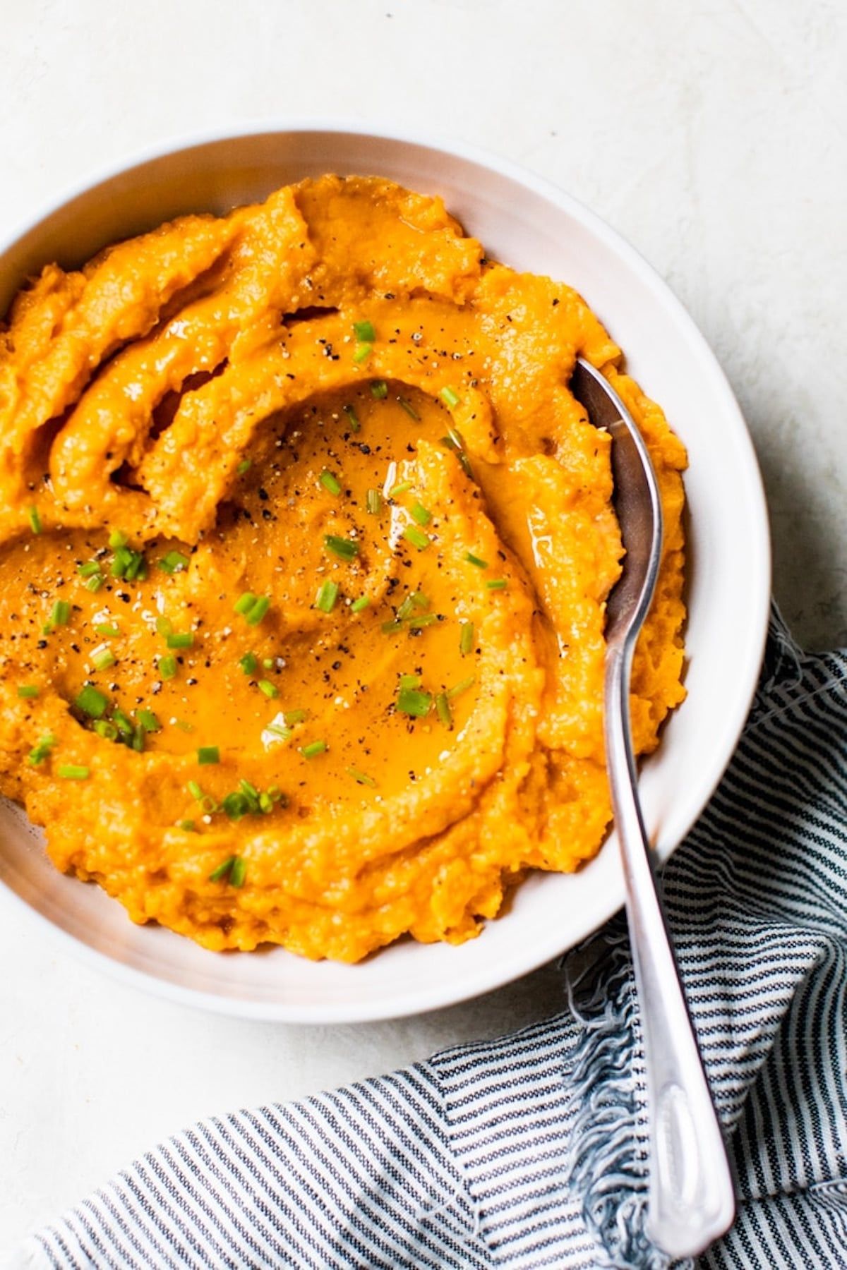 a white bowl of sweet mashed potatoes, with a spoon stuck in it