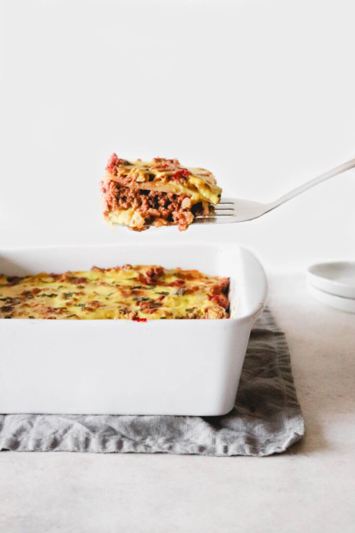 A white oven dish filled with lasagne with a fish slice lifting out a portion