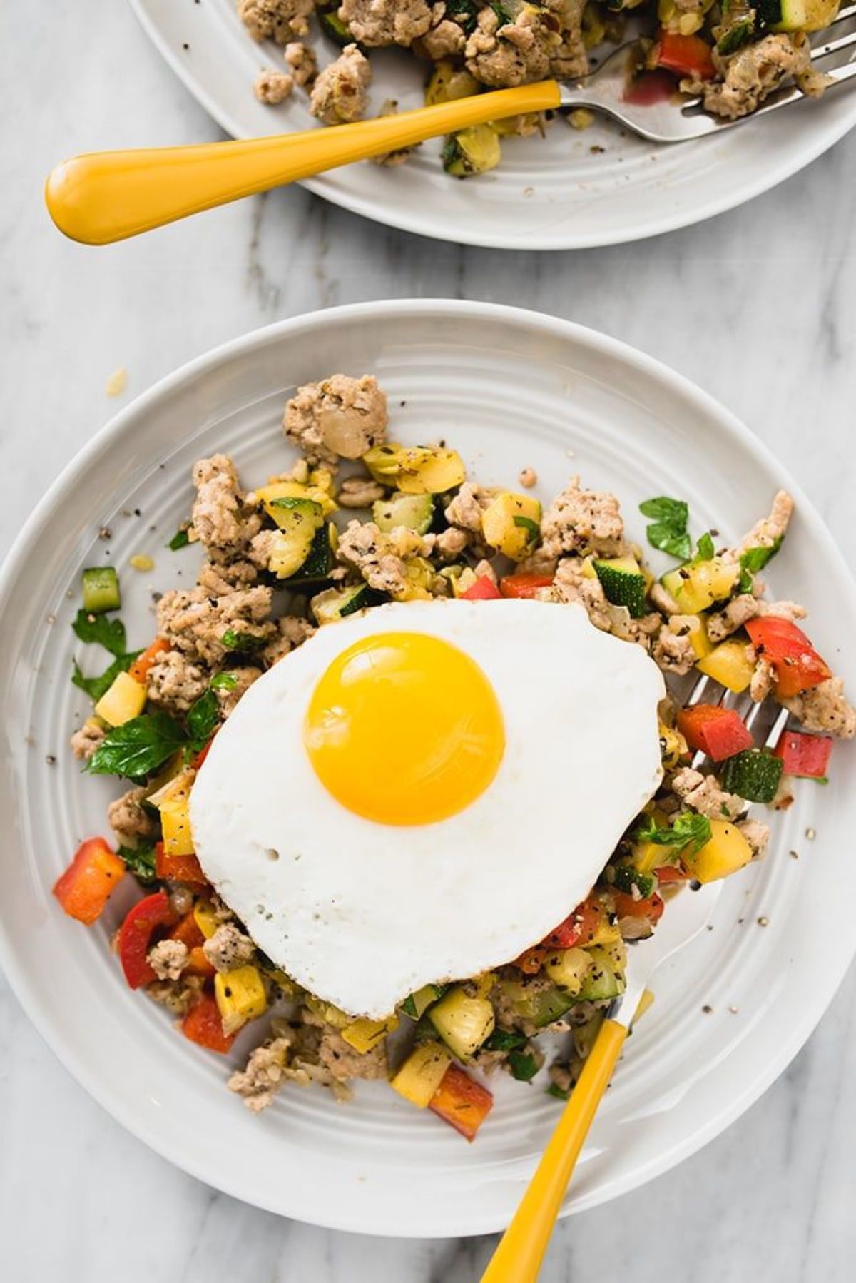 A white plate with turkey has on it, topped with a fired egg. A yellow handled fork is resting on the side