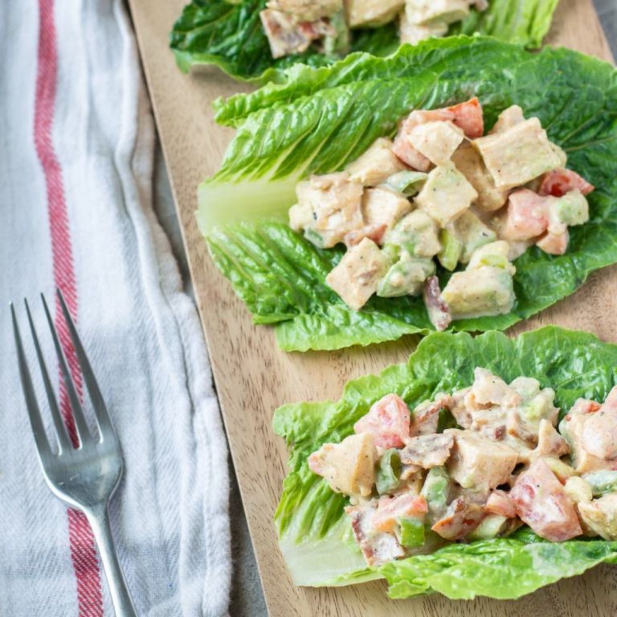 Lettuce cups on a wooden board with avocado BLT filling