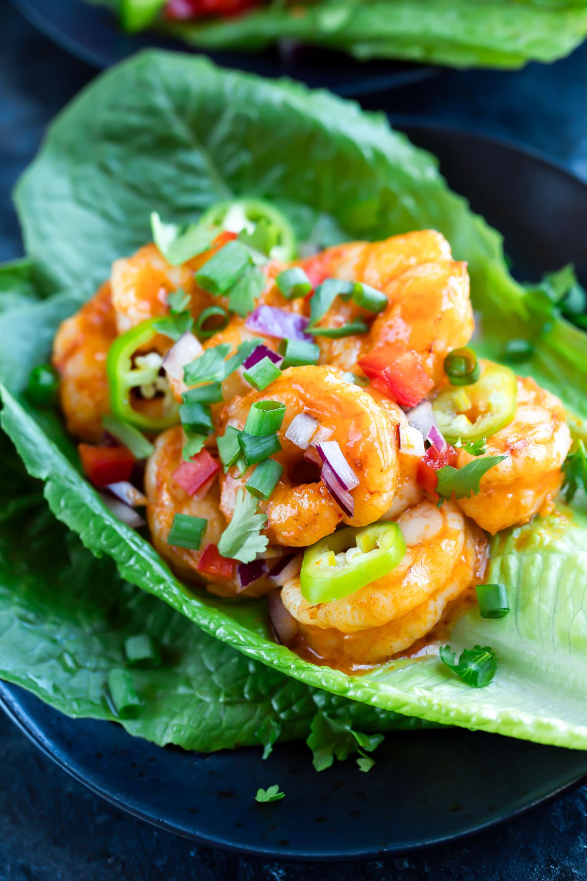 A close up of a lettuce cup filled with shrimp and sliced jalapenos sprinkled with chopped red onion and scallions