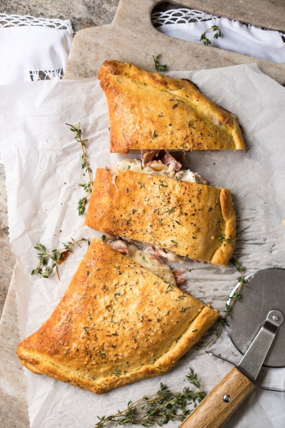 a calzone sliced into 3 pices with a pizza wheel on a baking parchmetn and board