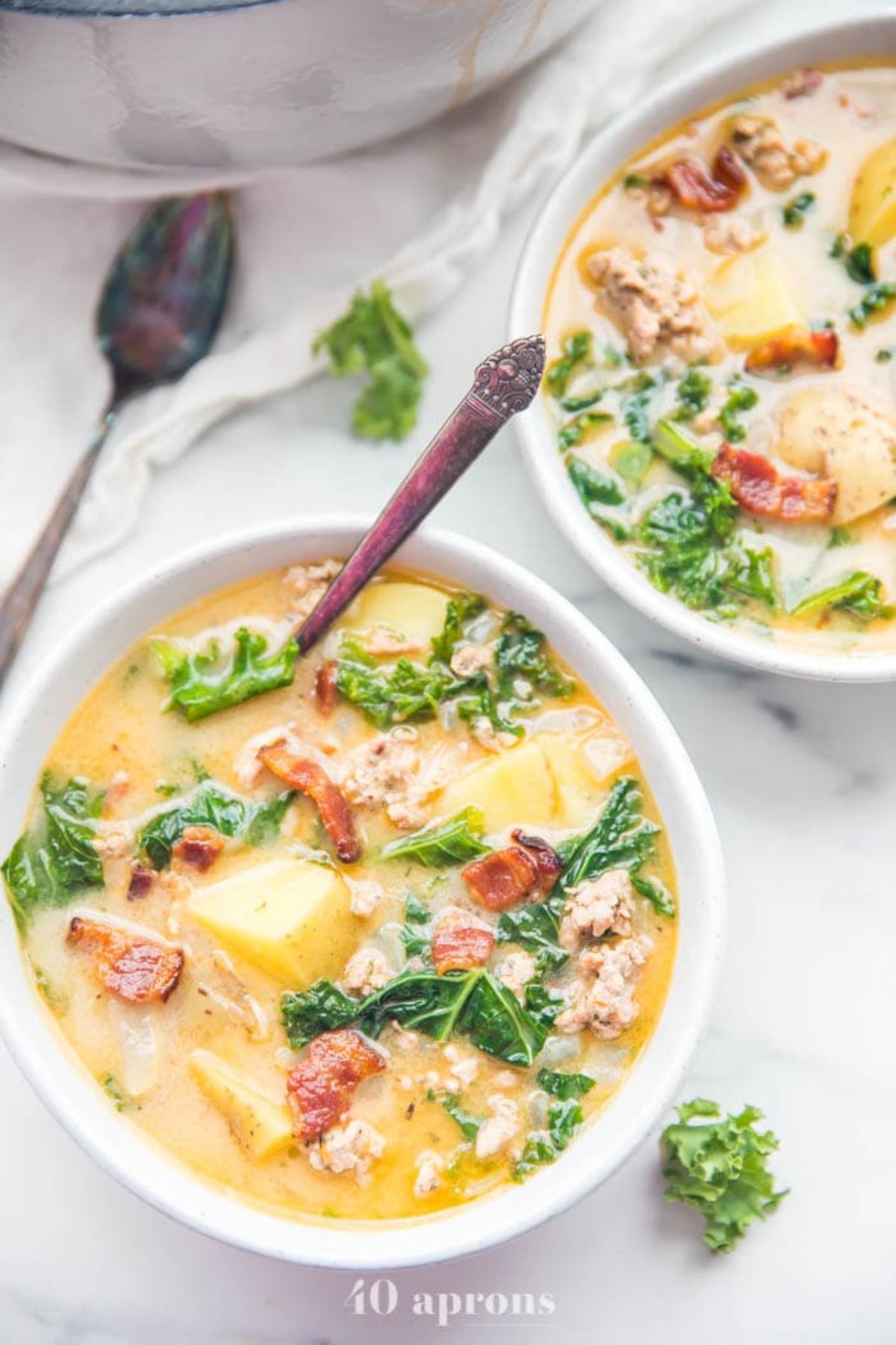 2 white bowls filled with tuscan sausage soup with a spoon sticking out of the one in front