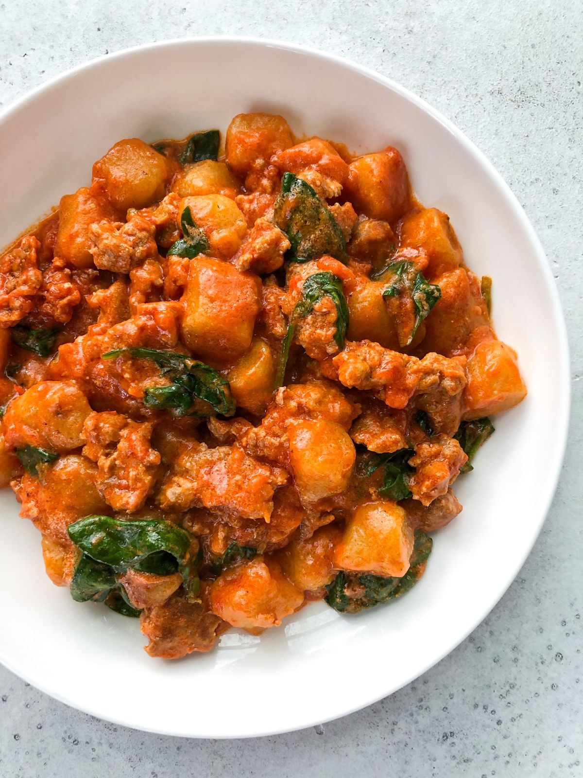 A white round bowl filled with gnocchi and beef in red sauce