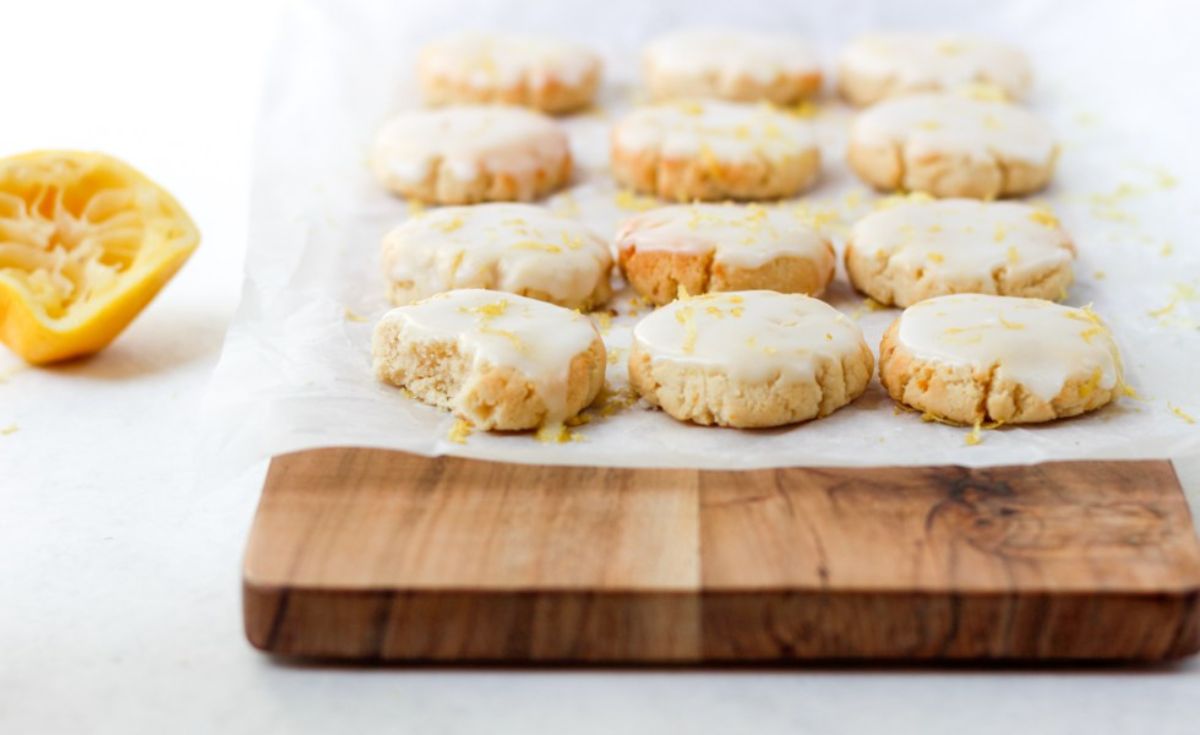 a wooden board with 12 iced lemon cookies on it, with a squeezed lemon half to one side