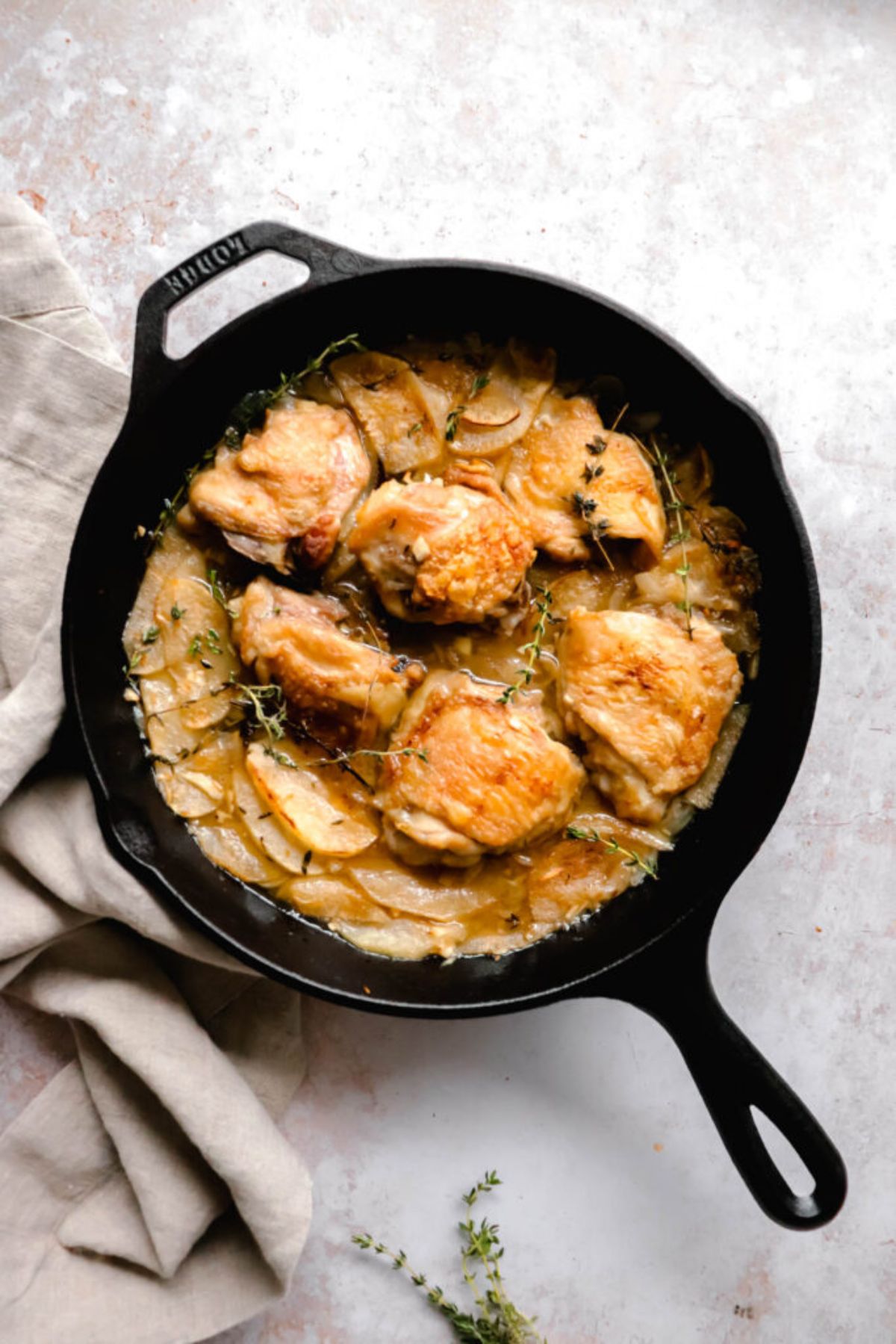 a skillet with chicken thighs, on a bed of sliced apples