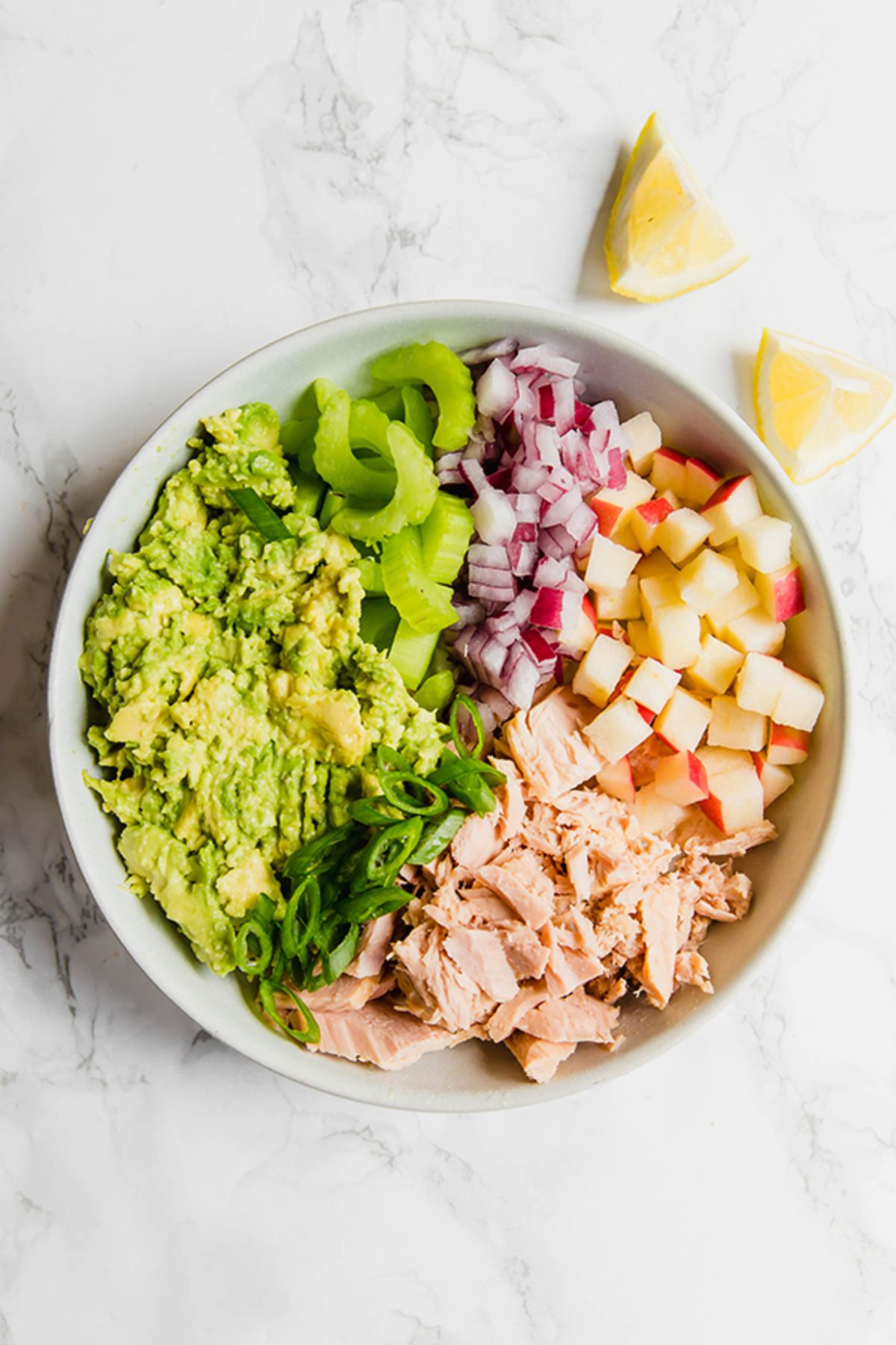 a bowl of avocado tuna salad with lemon wedges on the side