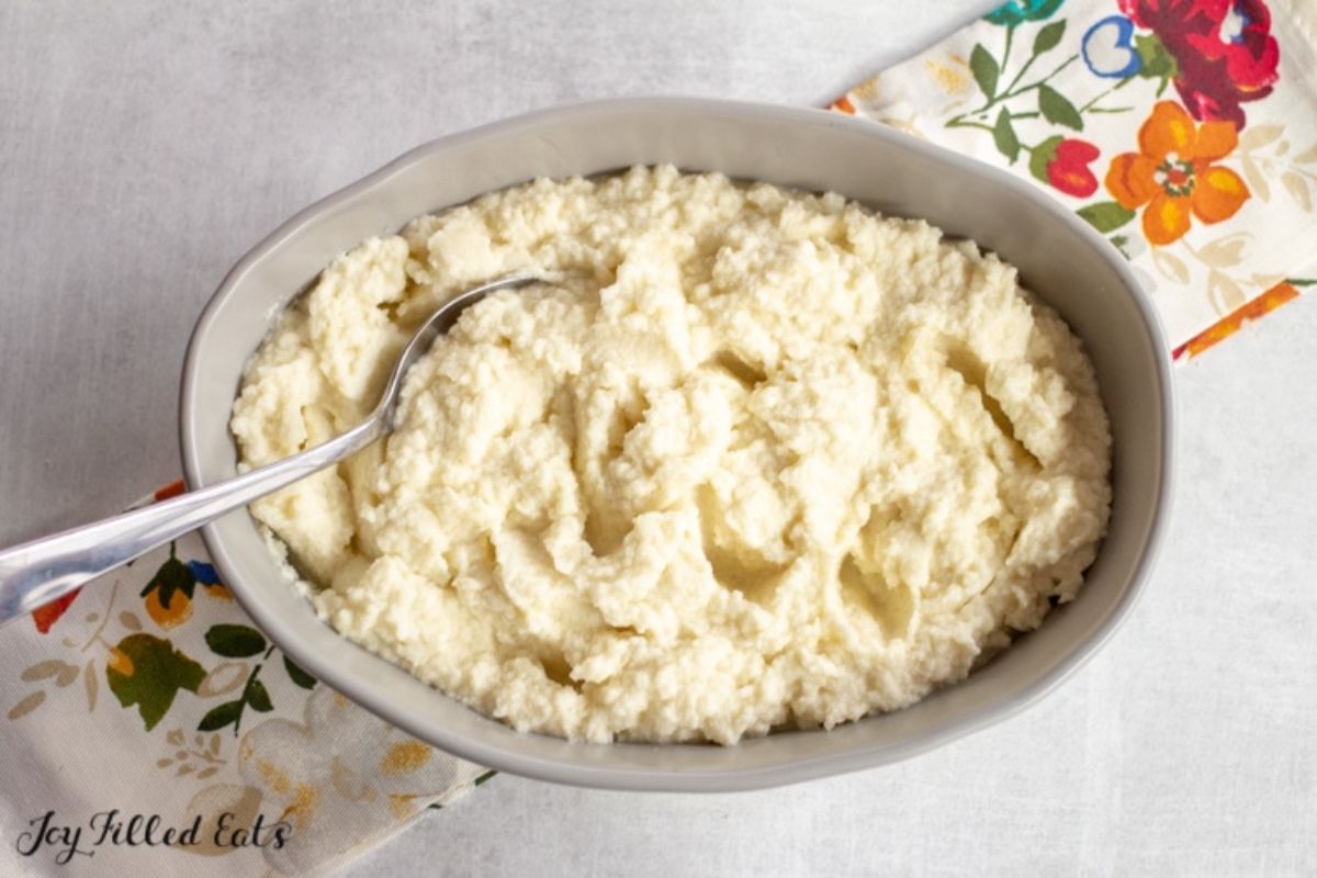 An oval dish filled with cauliflower mash and spoon sticking out of it