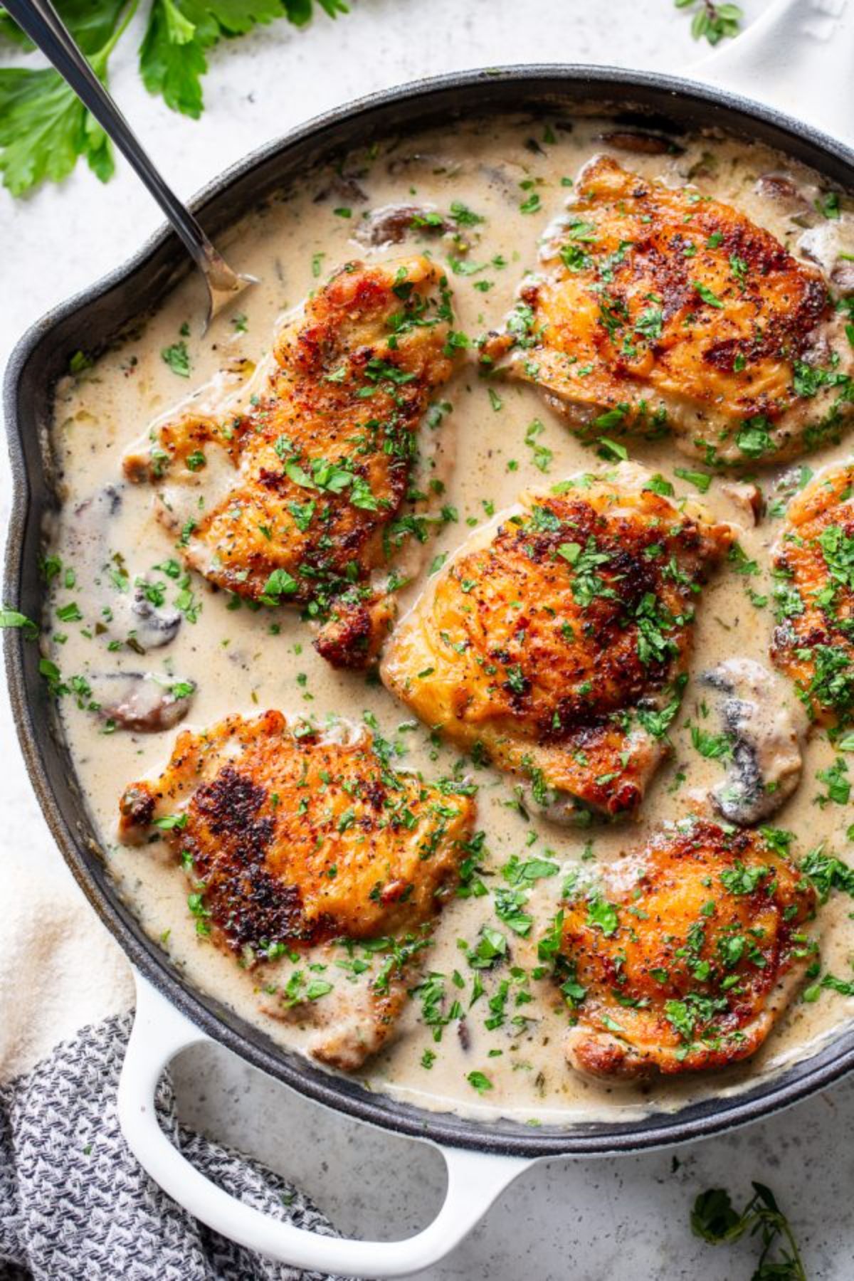 a skillet with chicken thigs in a garlic and herb sauce