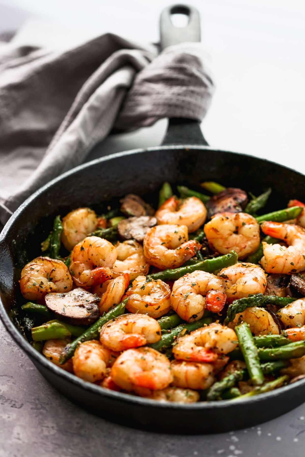 a cast iron skilllet with shrimp, asparagus and mushrooms inside