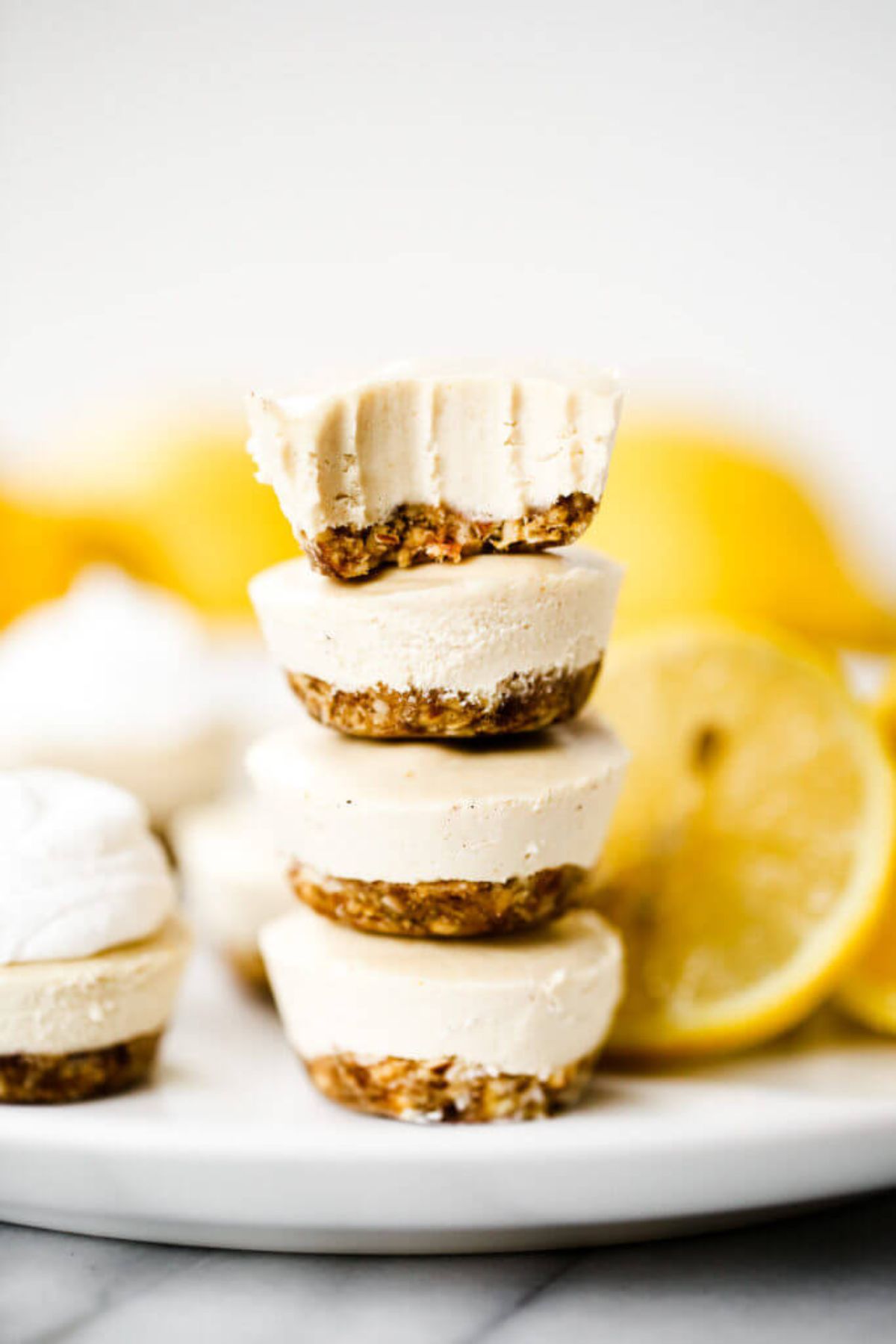 A plate with a pile of 4 lemon cheesecake bites on it. Lemon slices are behind