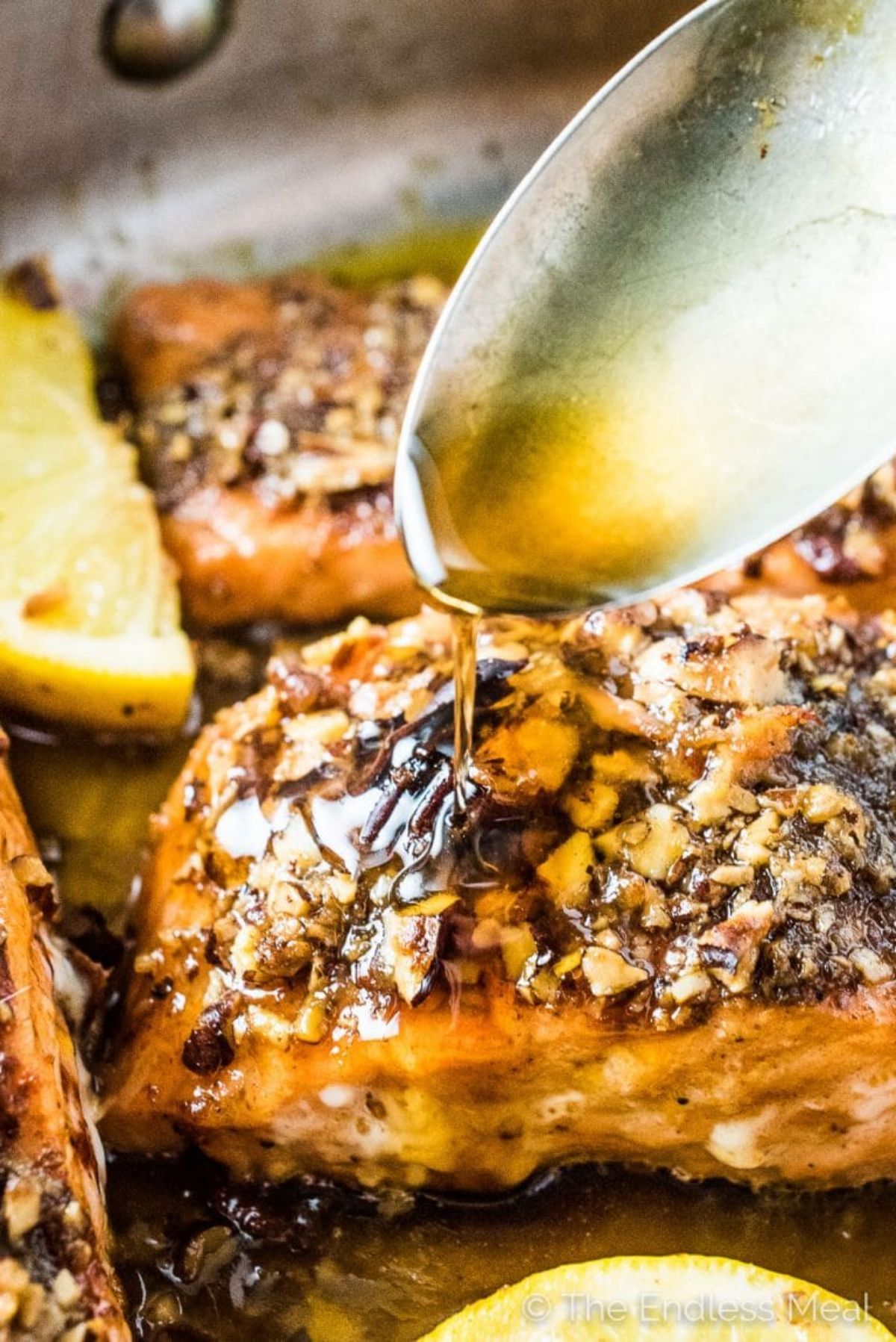 a partial shot of a baking tray with salmon fillets in, a spoon is drizzling oil over the top of one fillet