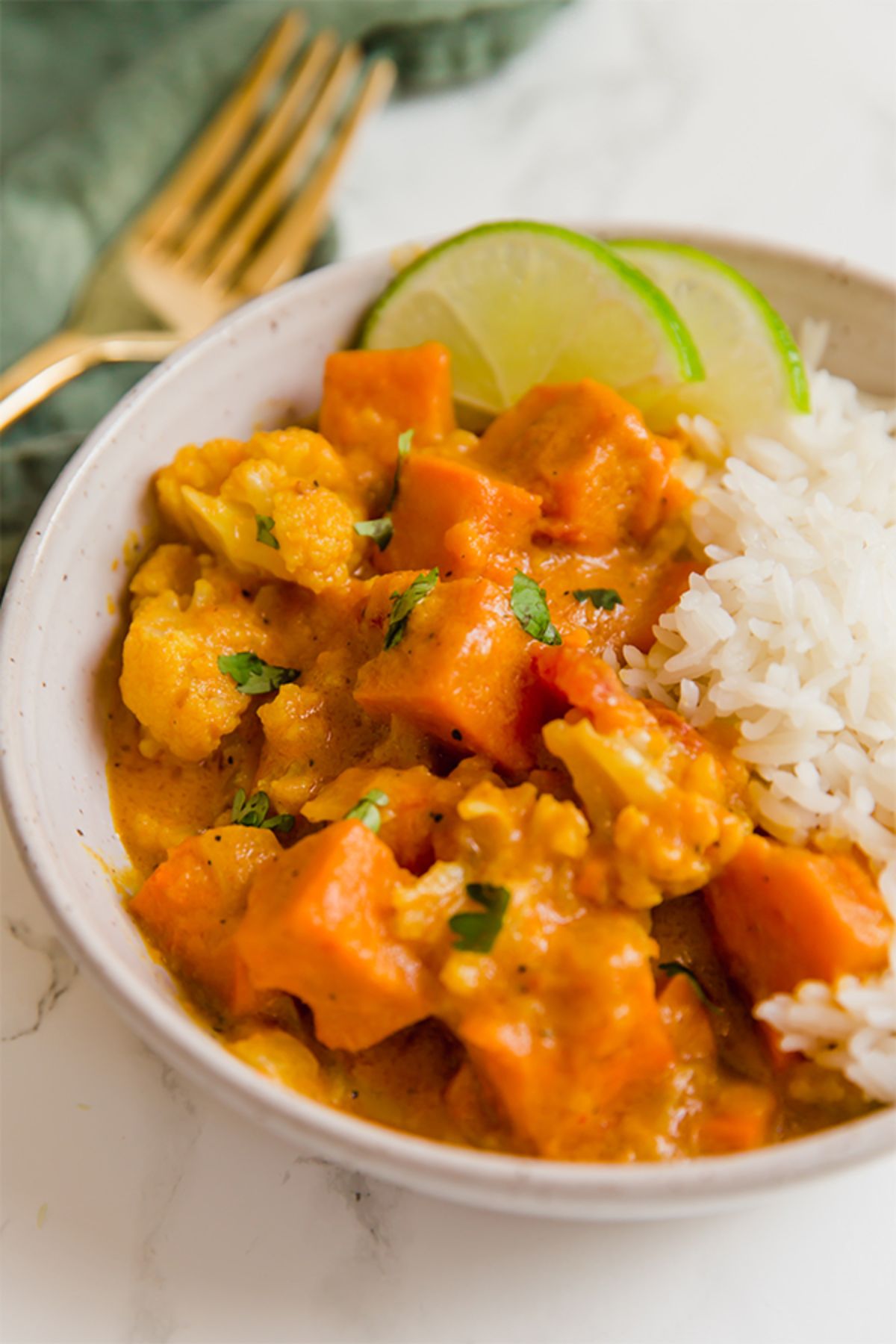 A white bowl of sweet potato cauliflower curry with lime slices and rice.