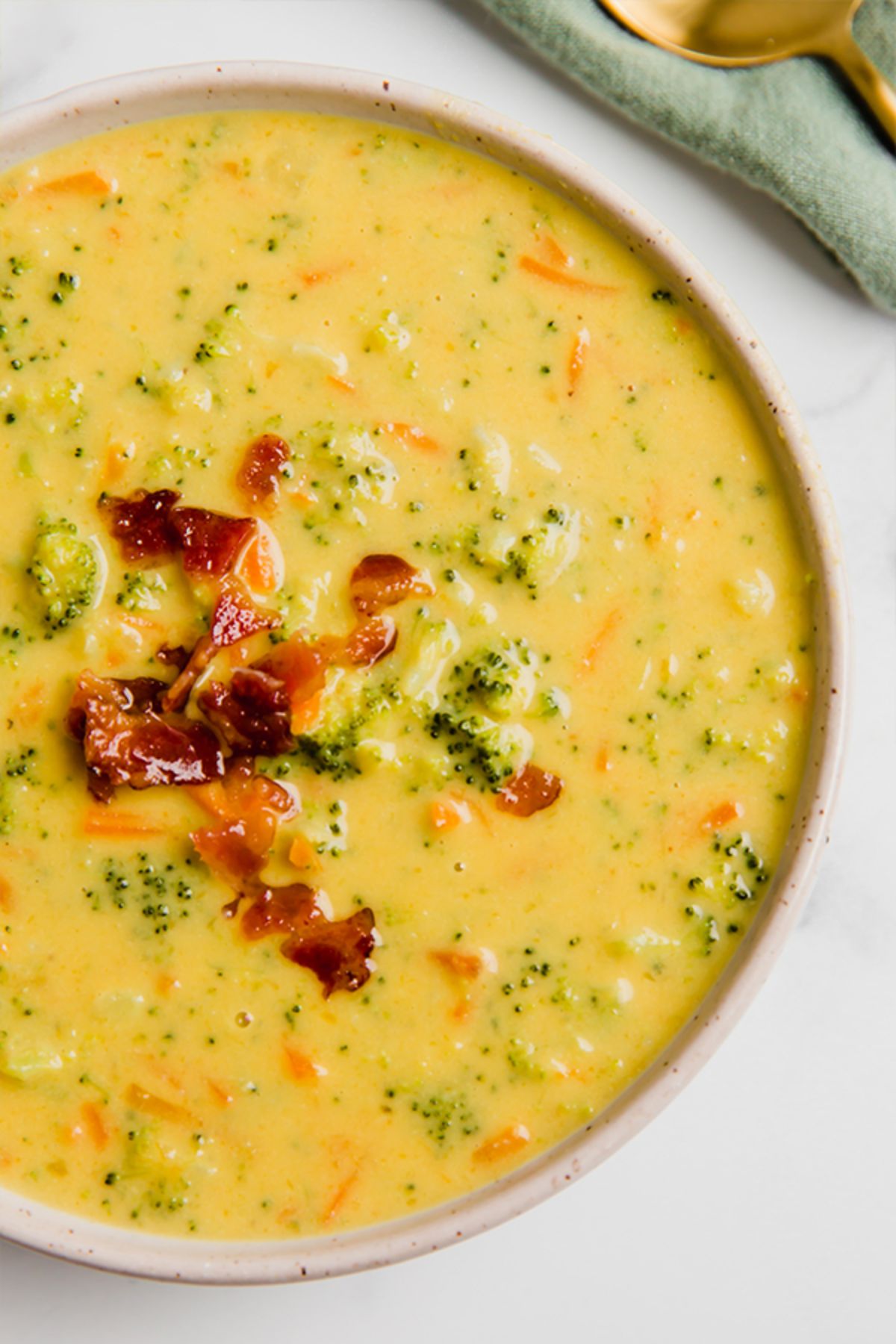 a bowl of yellow soup with broccoli florets just seen, and topped with crispy bacon bits