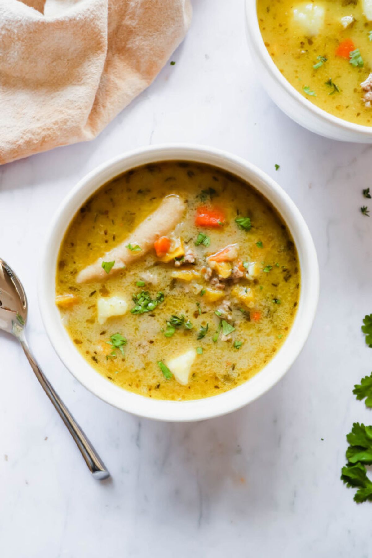 A white bolwl with an orange soup scattered with herbs.