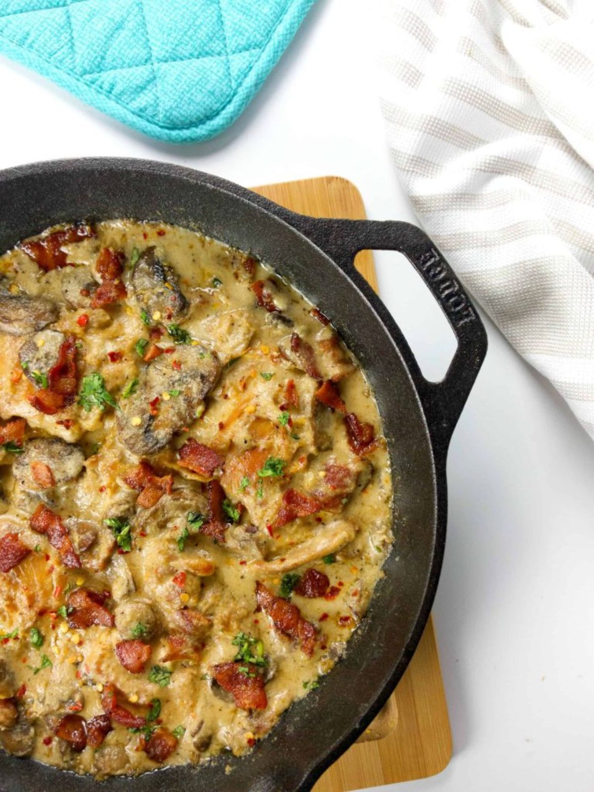 A cast iron skillet with chicken in sauce in it on a wooden board