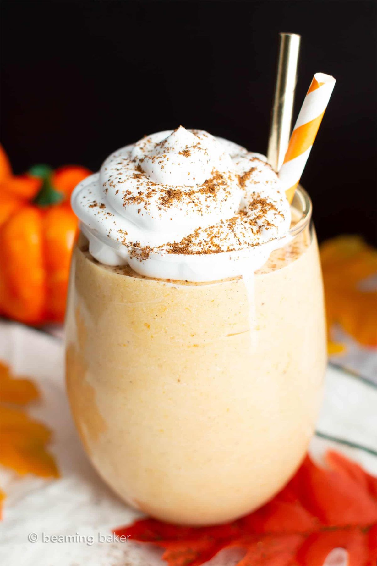 A glass with a pumpkin pie smoothie in it, topped with whipped cream and sprinkled with cinnamon. Two straws are in the glass