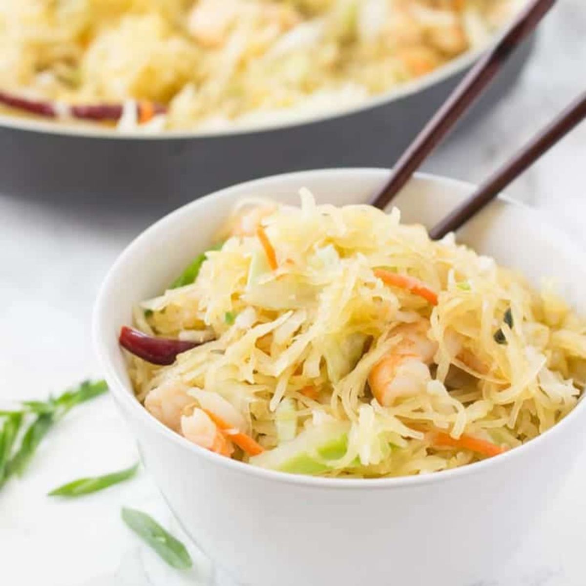 White bowl filled with noodles, shrimp and vegetables. Chopsticks are stickign out of the bowl