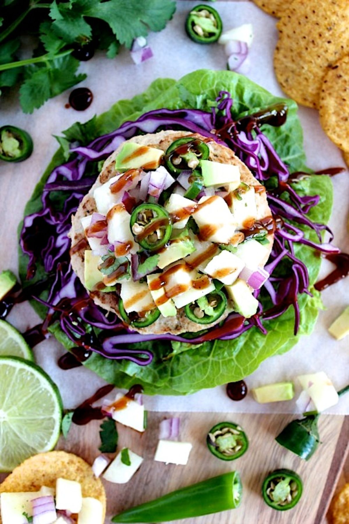 A lettuce leaf acts as a platter for a turkey burger topped with cheese, jalapeno slices and a brown sauce. Ingredients are scattered around it