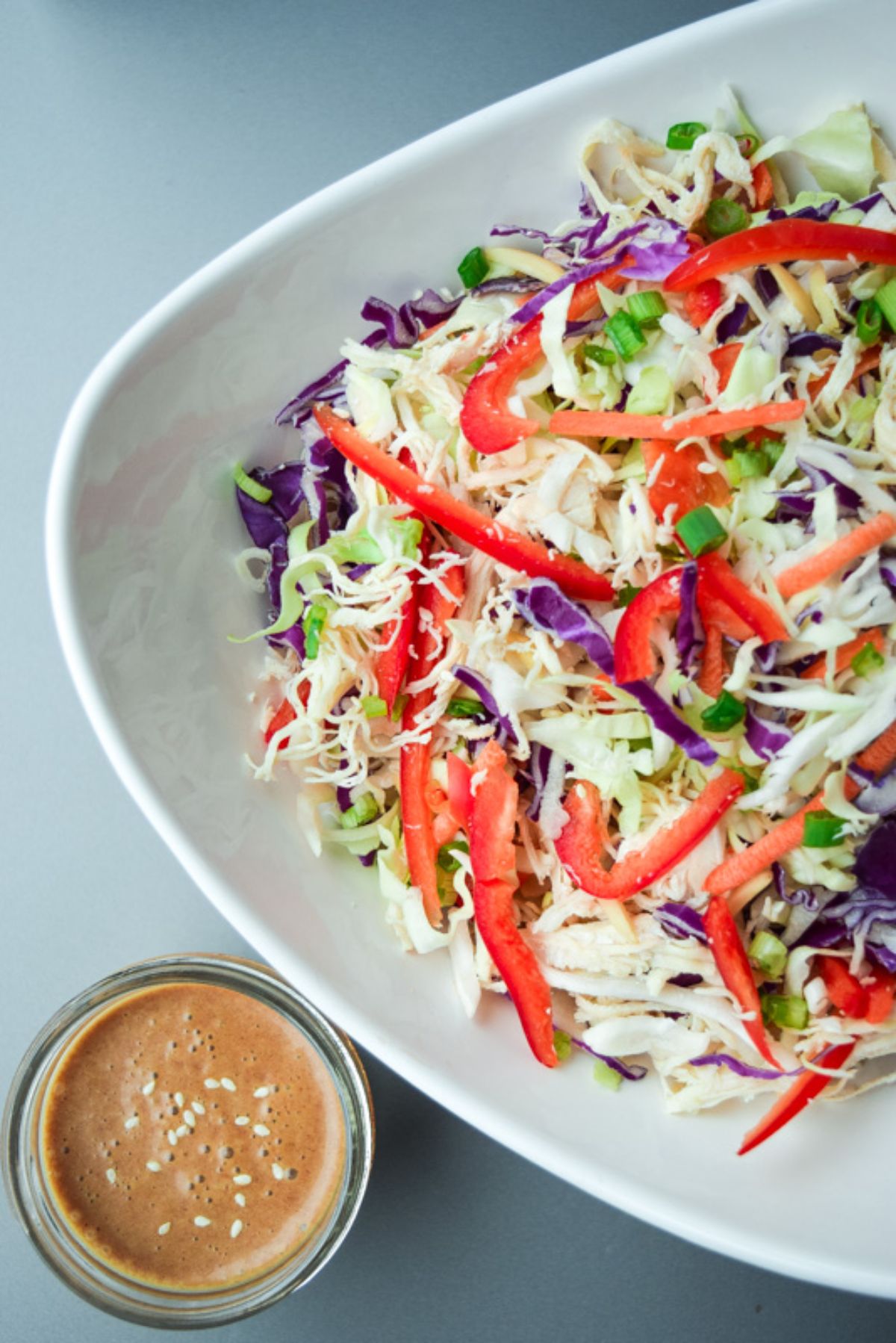 a partial shot of a white bowl of chopped asian chicken salad and a small pot of dressing