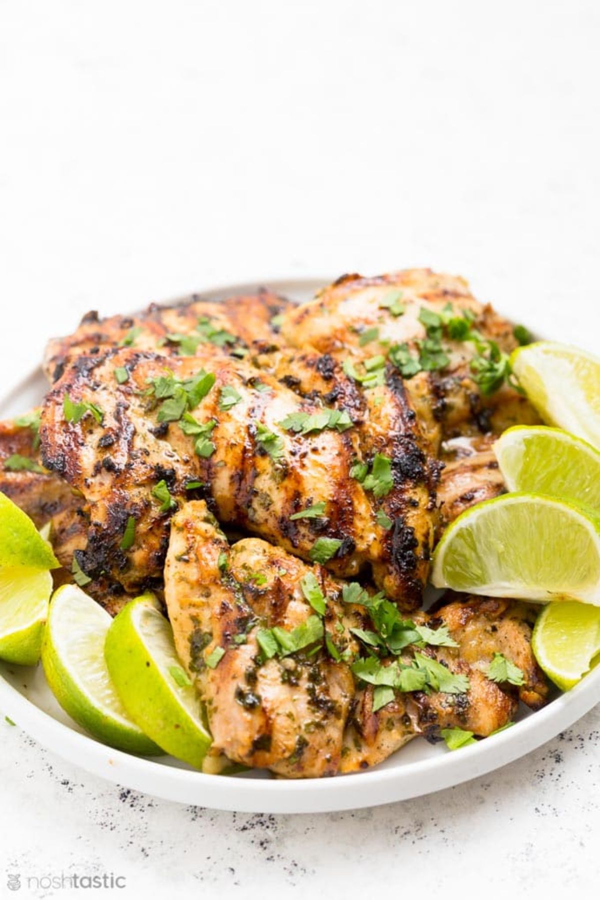 A plate of roasted chicken thighs garnished with chopped herbs and lime wedges