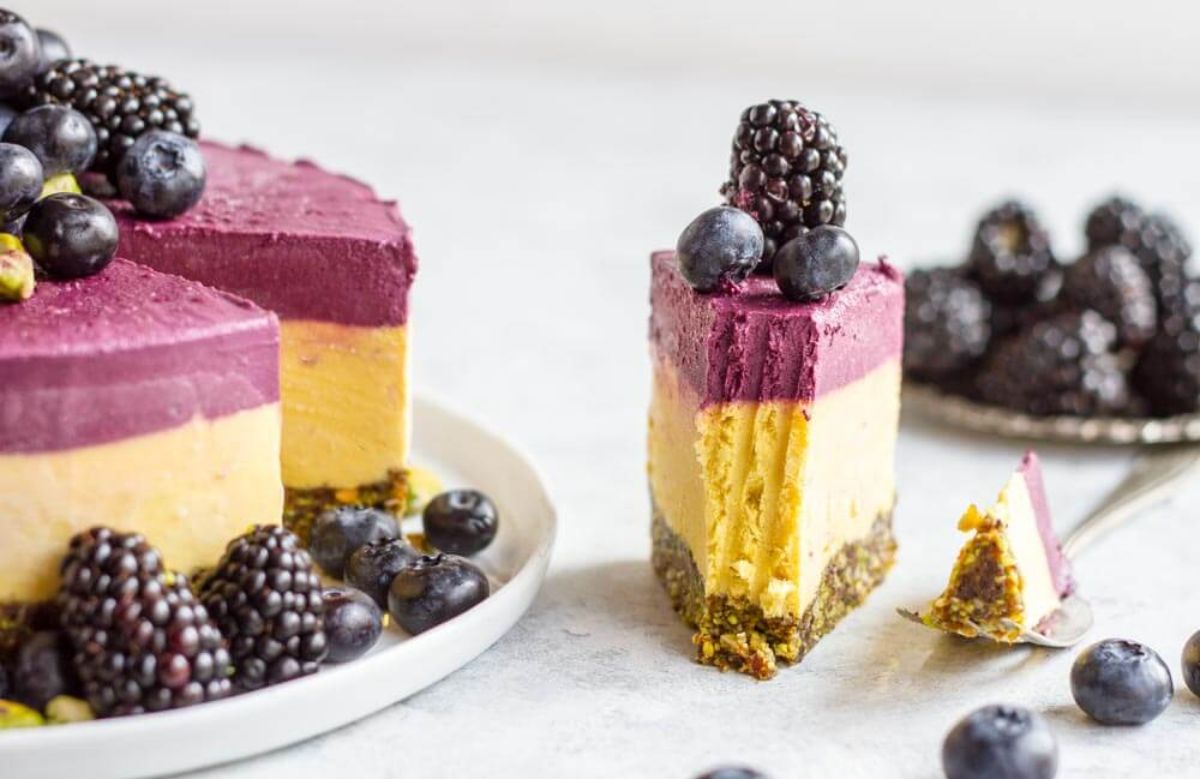 a layered cheesecake, with a biscuit base, mango layer, and blackberry layer. Topped with fresh fruit