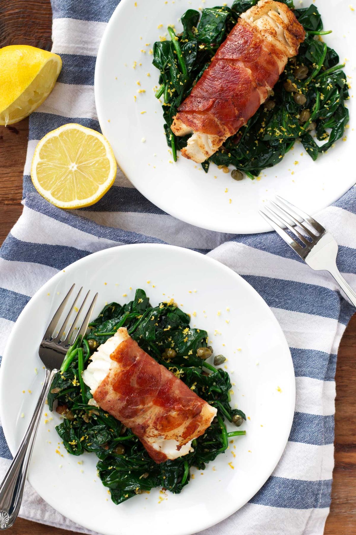 2 plates of proscuitto-wrapped cod on a bed of spinach