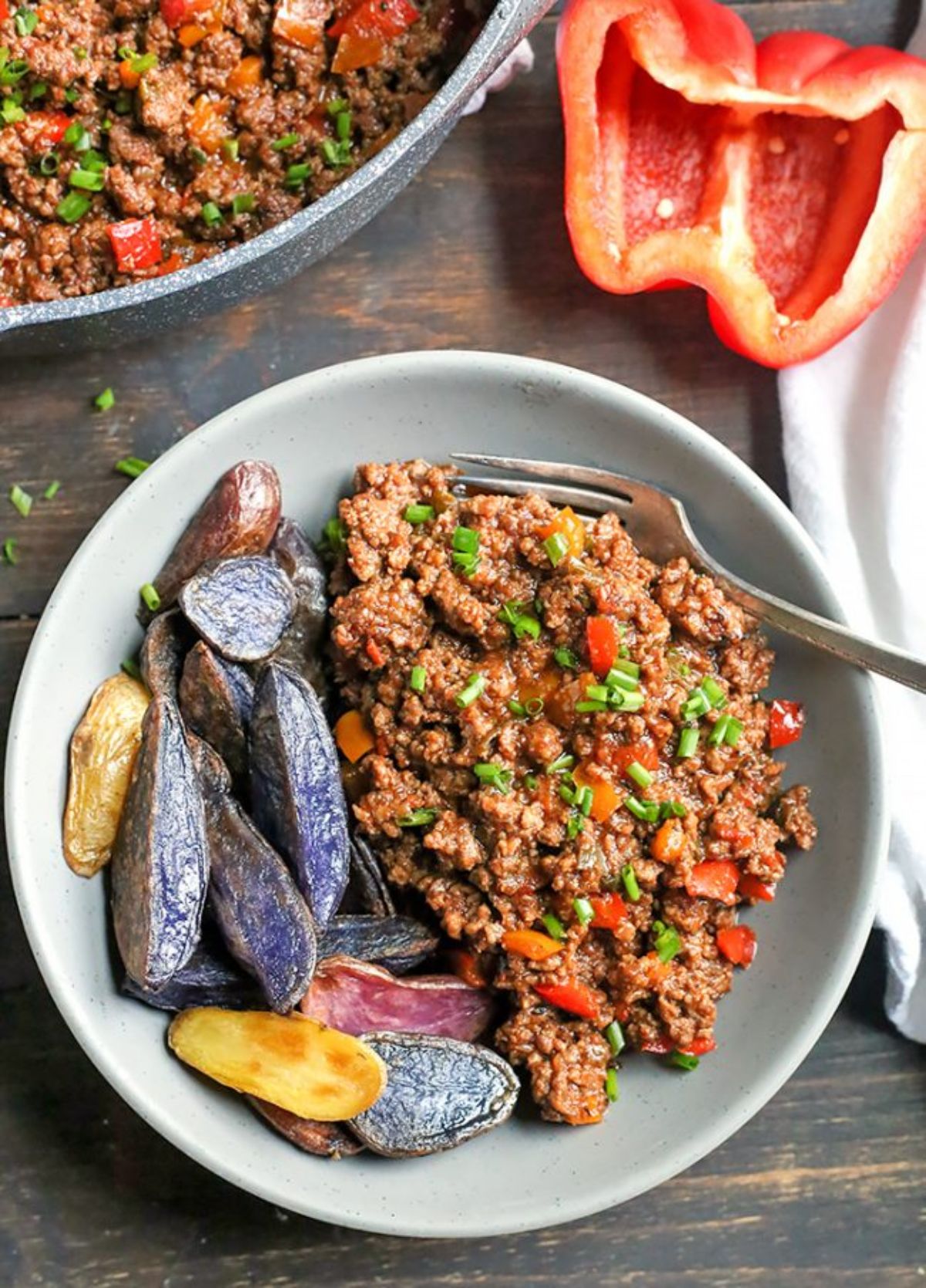 a white bowl with ground beef in a sauce on one side and potato wedges on the other