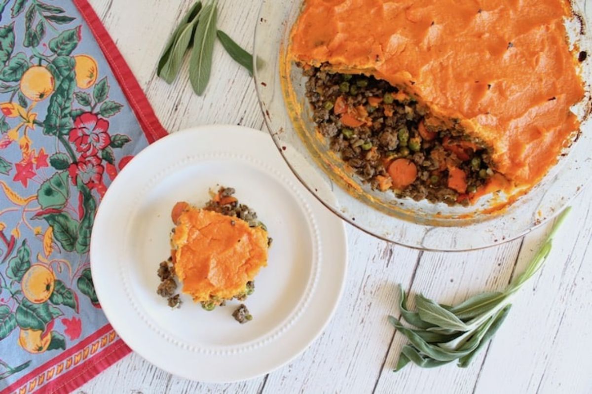 a glass casserole dish with sweet potato shepherd's pie. next to it is a small plate with a portion of the pie on it