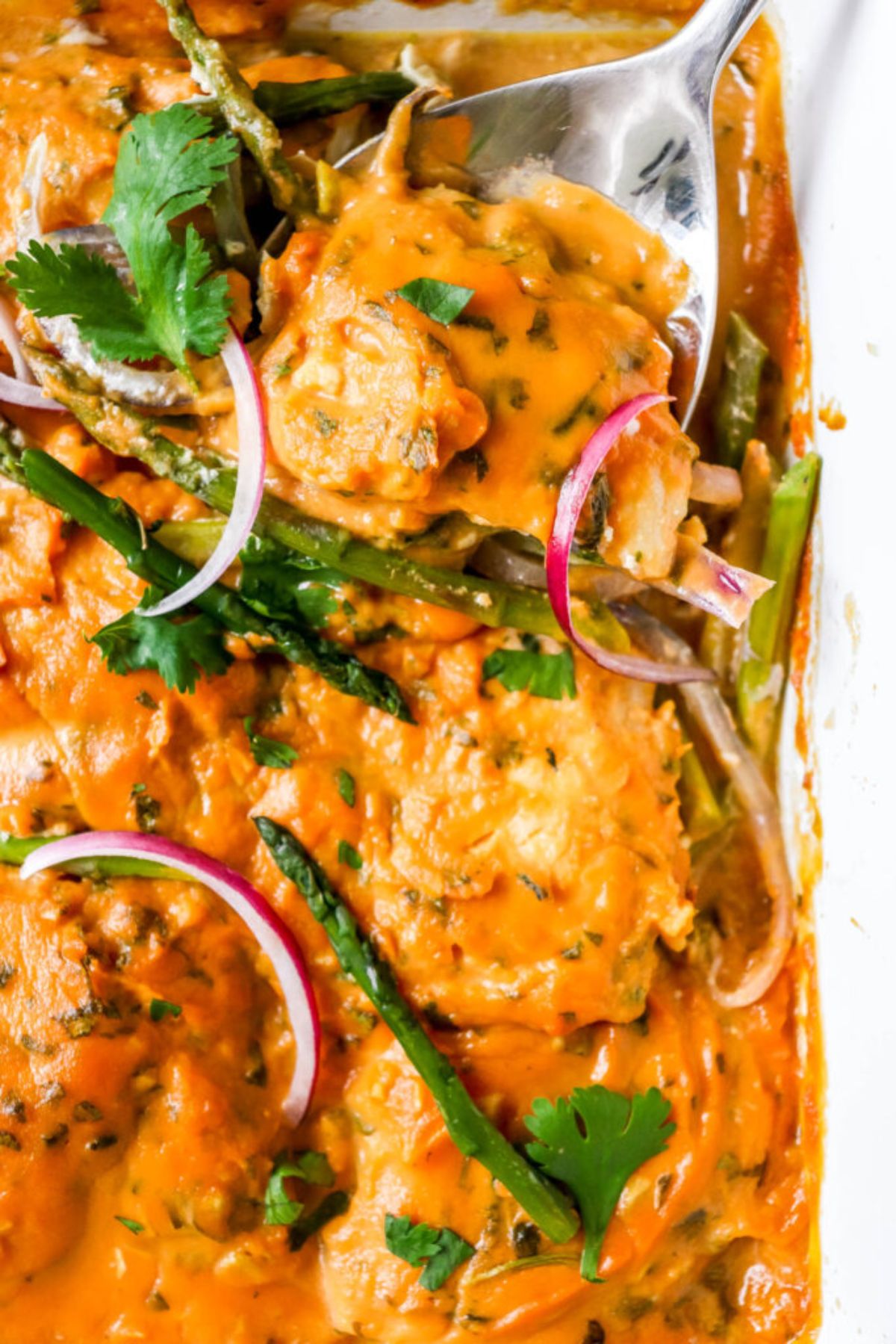 a partial shot of a casserole dish with baked haddock in sweet potato sauce. asparagus spears and red oinion slices can be seen