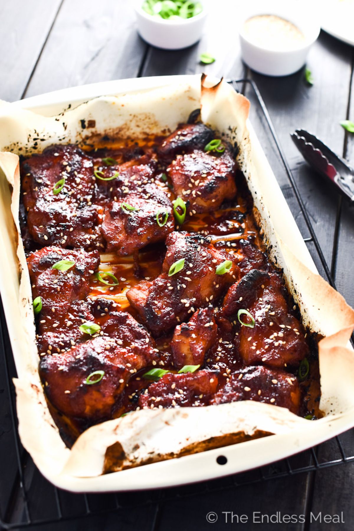 A paper-lined baking tray filled with korean chicken thighs and topped with sliced scallions and sesame seeds