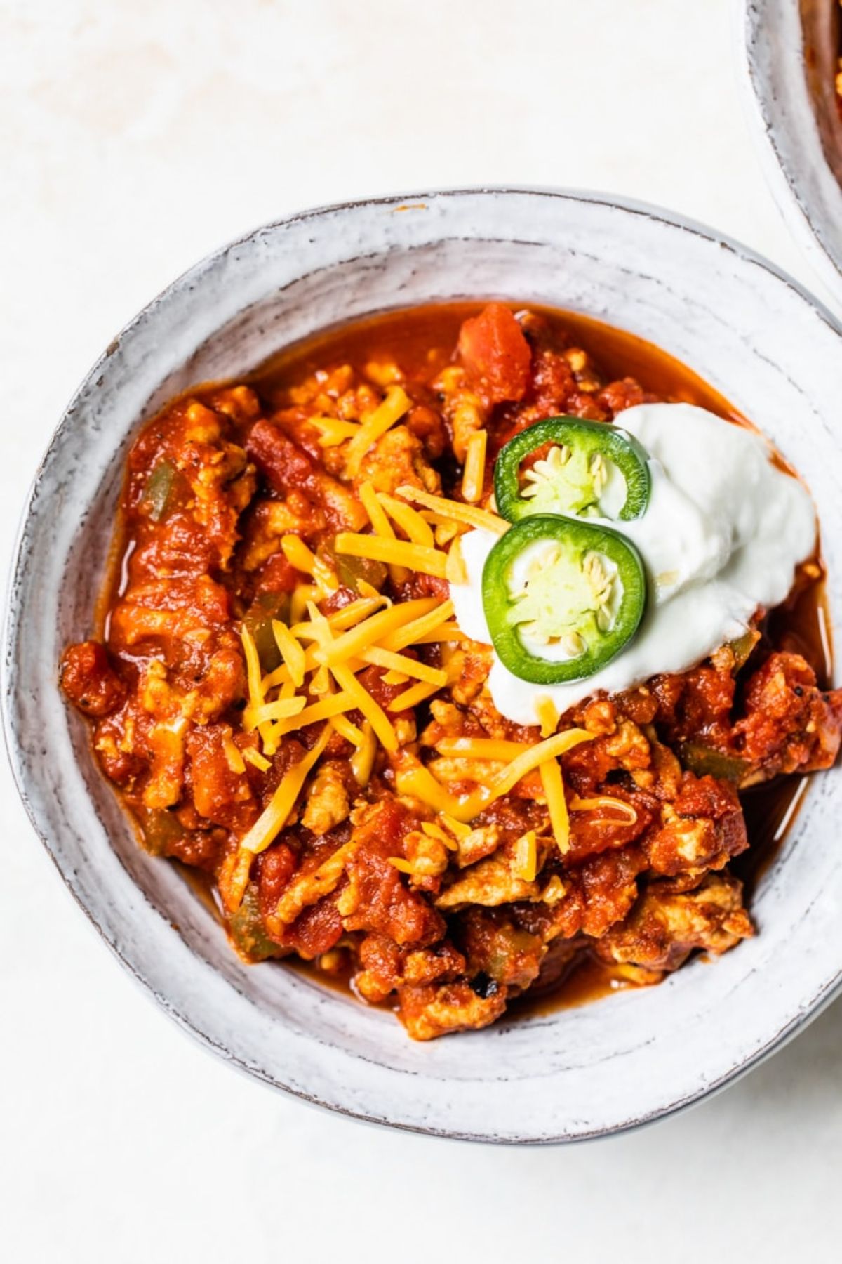 A bowl of chilli topped with grated cheese, sour cream and sliced Jalapenos