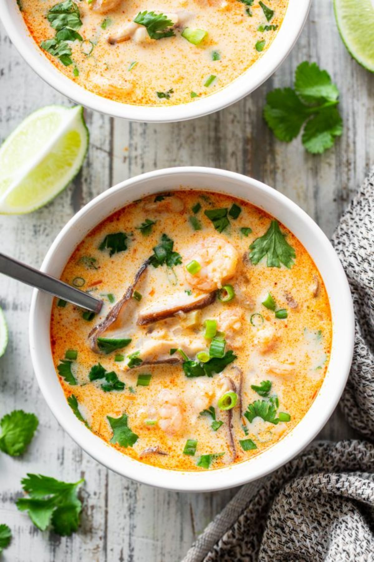 a white owl of creamy shrimmp soup wiht sliced scallions and herbs sprinkled over the top. The bowl is surrounded by lime wedges and cilantro