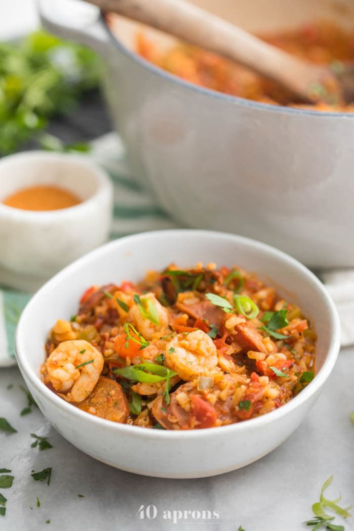 a white bowl of jambalaya, with a large pot of the same dish behind it