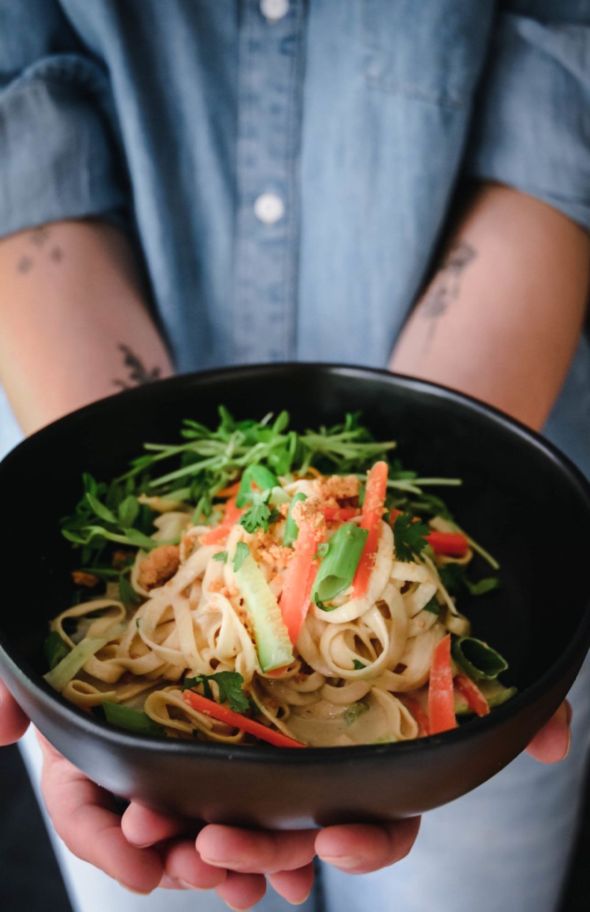 Two hands hold a black bowl containing rutabag oodles, and spiralized vegetables