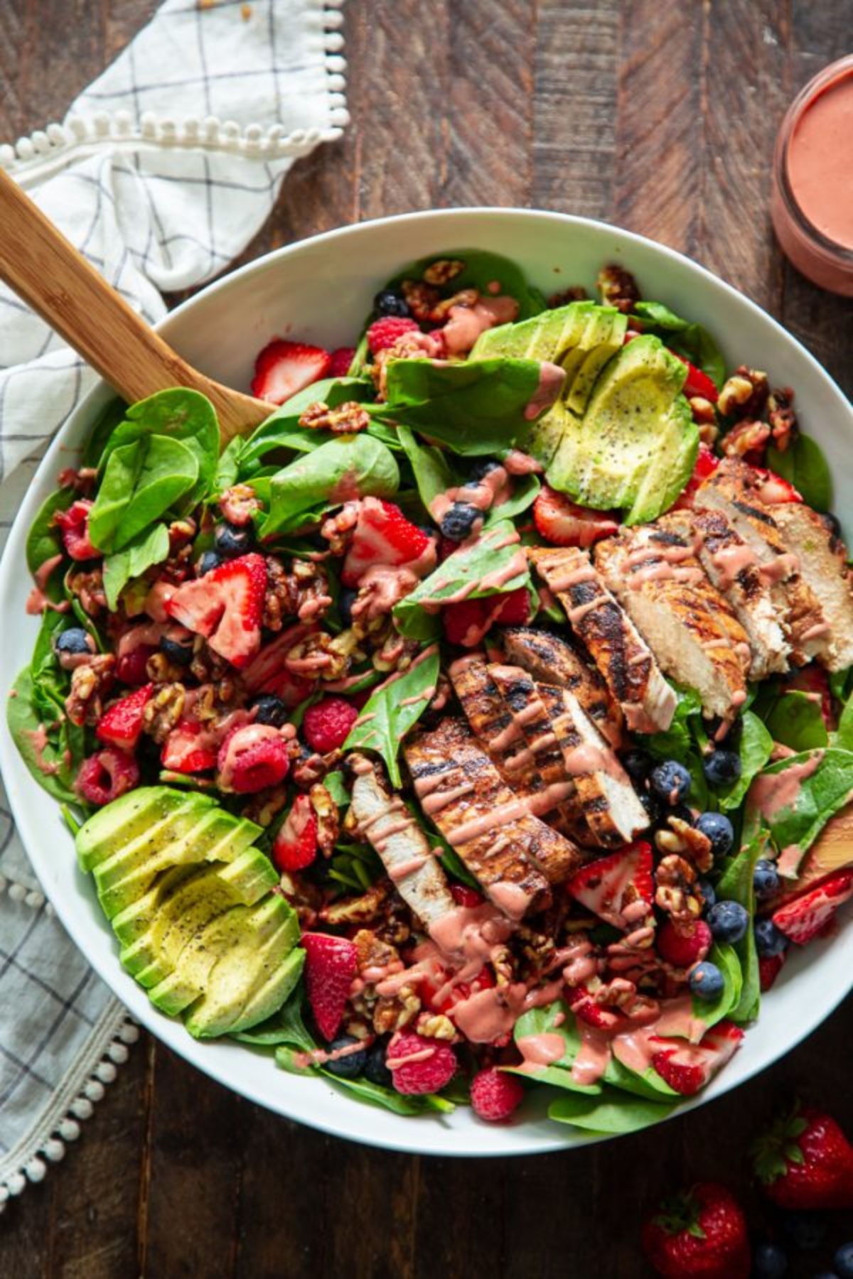 a white bowl of chicken, avocado, leaves and berries