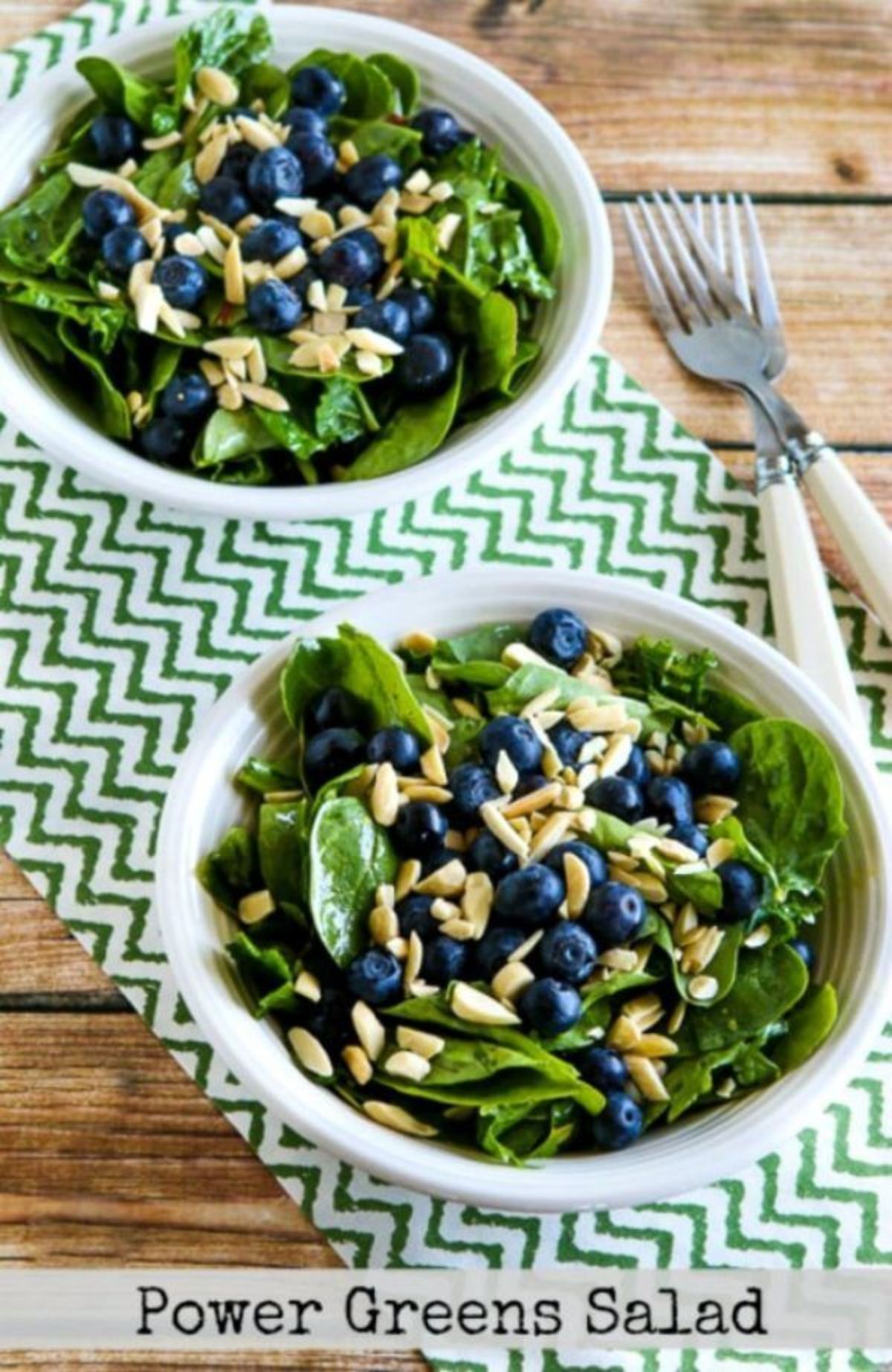 2 white bowls of green leaves, blueberries and chopped nuts, 2 forks by the side