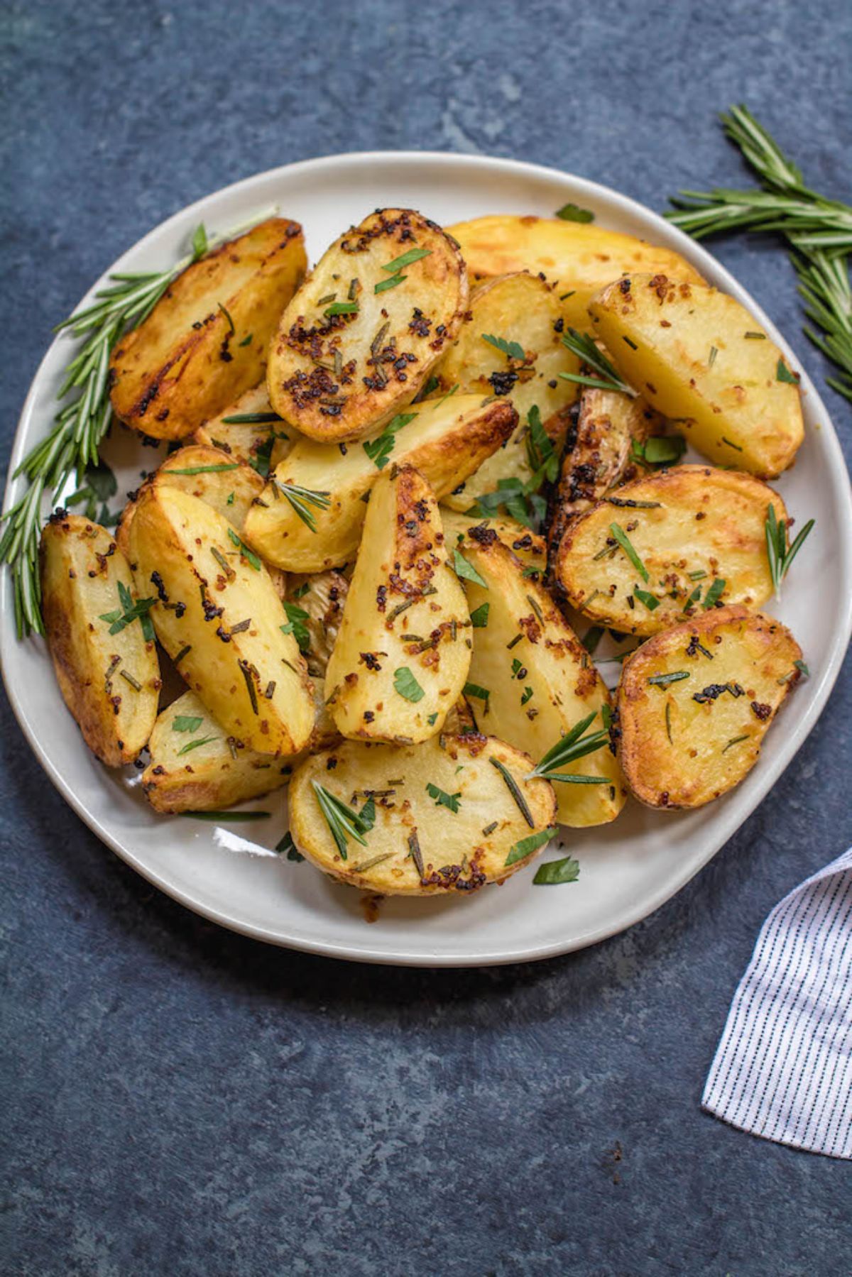 A whote plate of roasted potatoes scattered with rosemary sprigs