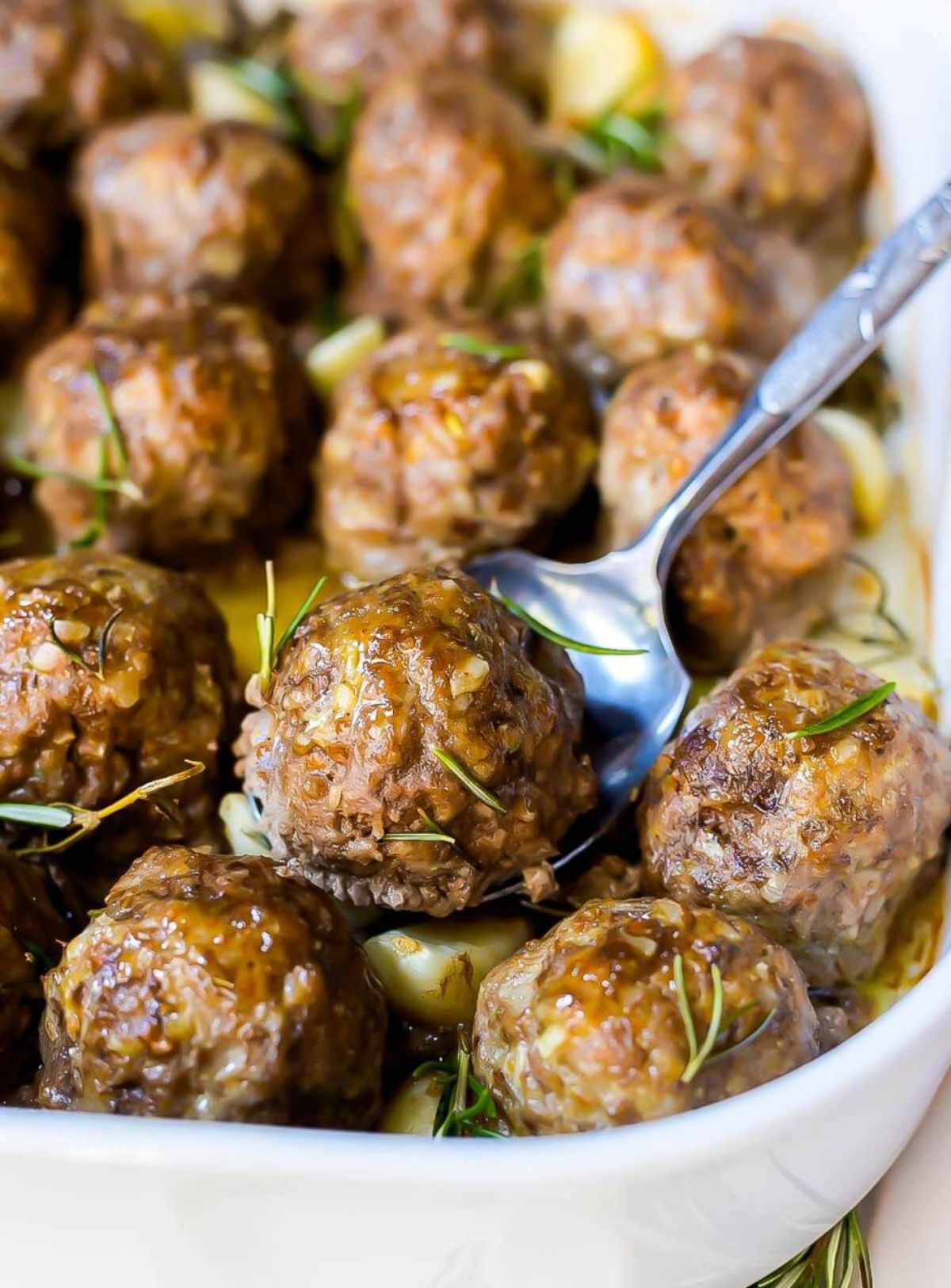 A close up of a dish of meatballs with a spoon lifitng one of them out