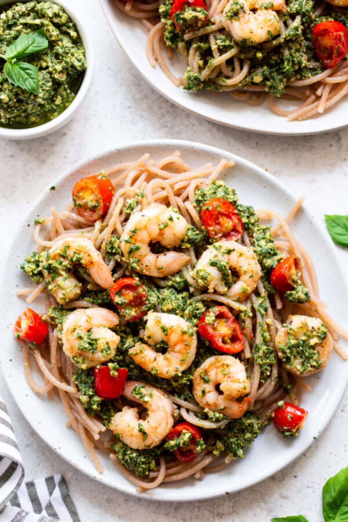 a plate full of noodles, shrimp and plum tomatoes drizzled with pesto sauce.
