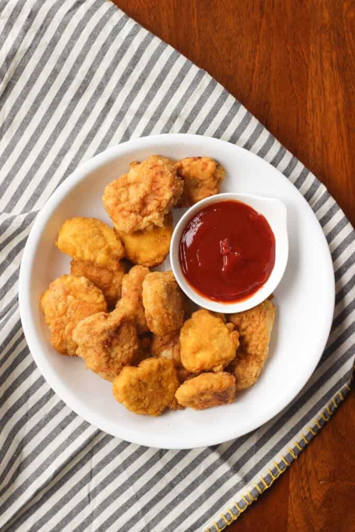 A white plate of chicken nuggets with a smaller bowl of red sauce