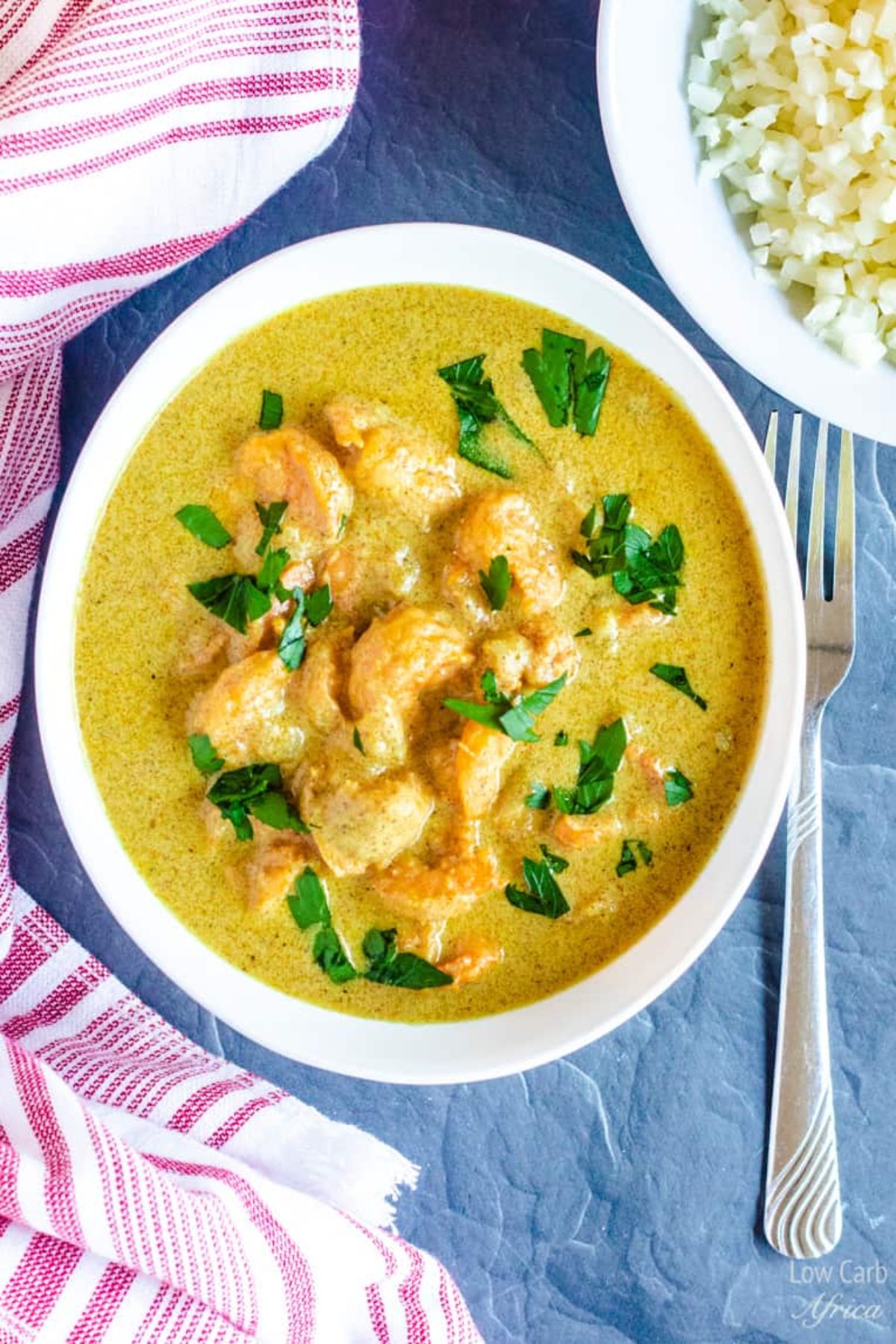 a white dish of shrimp curry garnished with chopped herbs