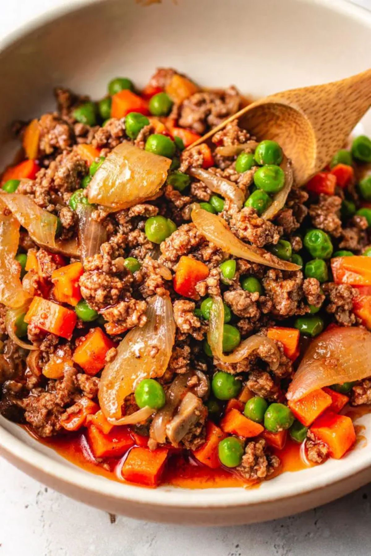 A bowl of ground beef and vegetables in sauce with a wooden spoon sticking into it