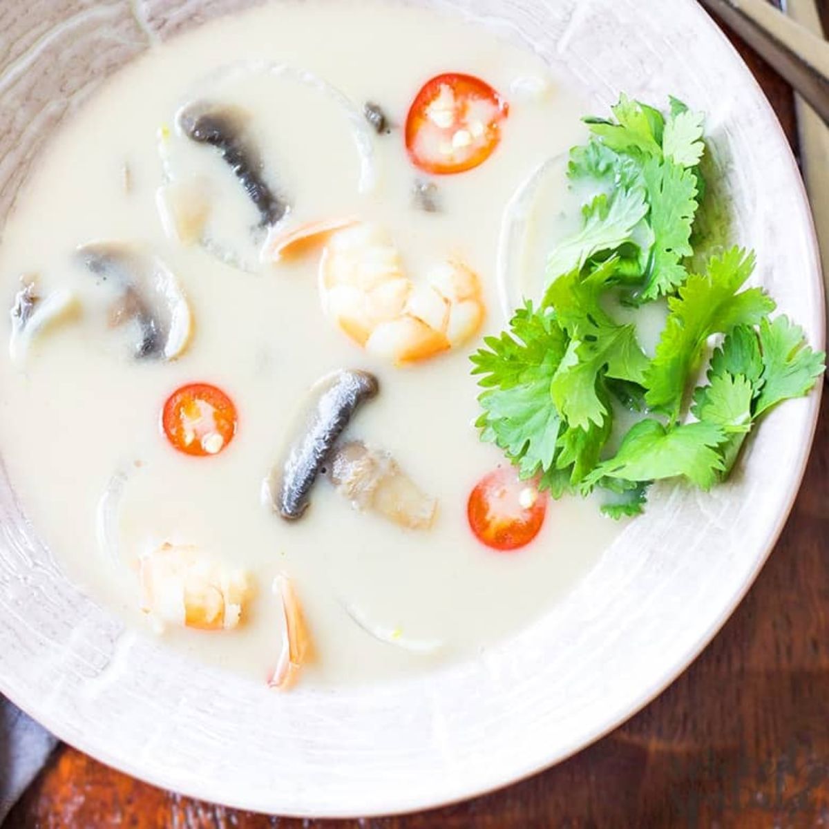 a white bowl of tom kha gai garnished with coriander