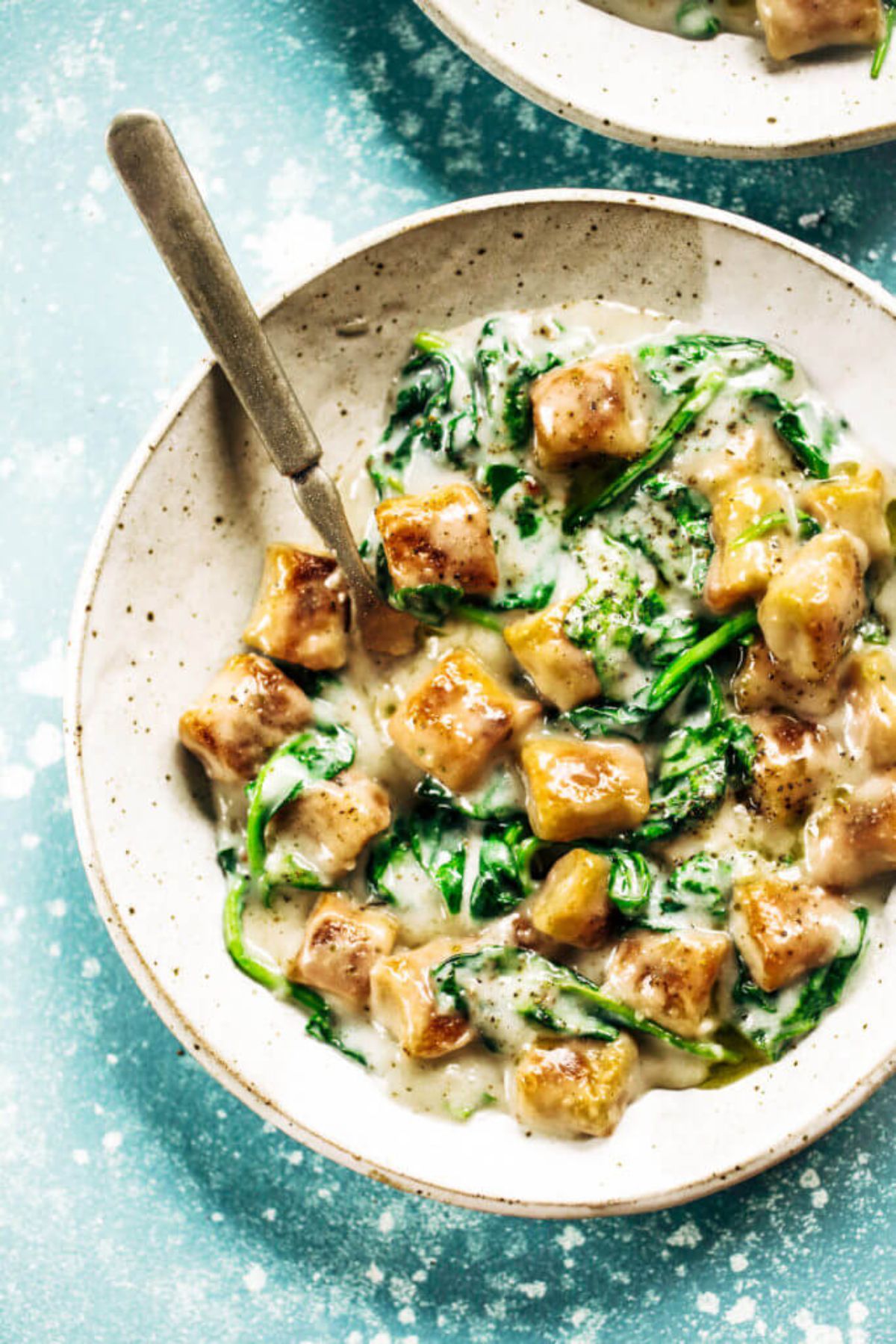 a white speckled bowl of cauliflower gnocchi and spinach in a creamy sauce
